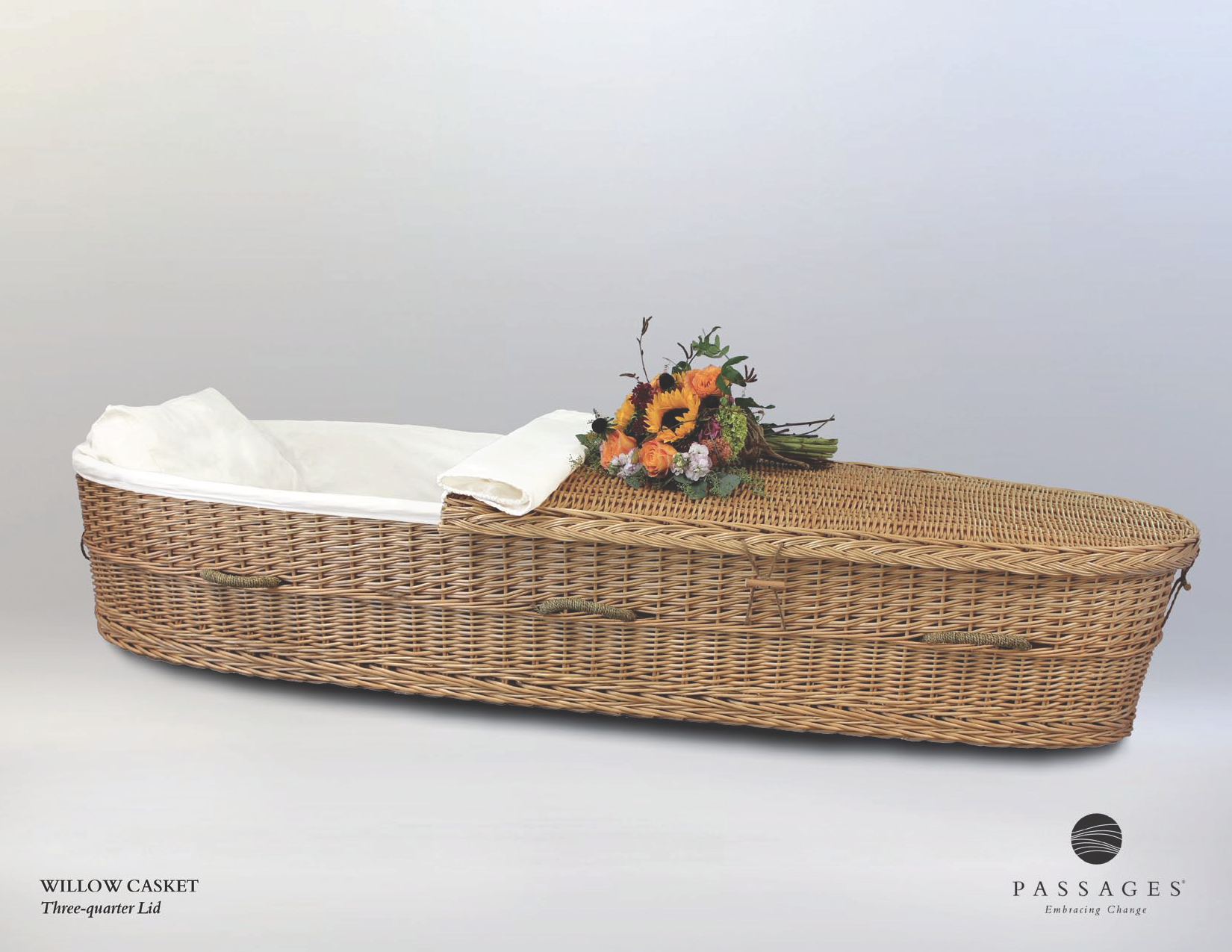 Wicker coffin with white lining and floral arrangement, studio shot.