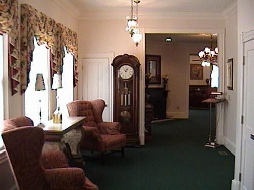 A formal interior with seating, a grandfather clock, and a doorway leading to another room.