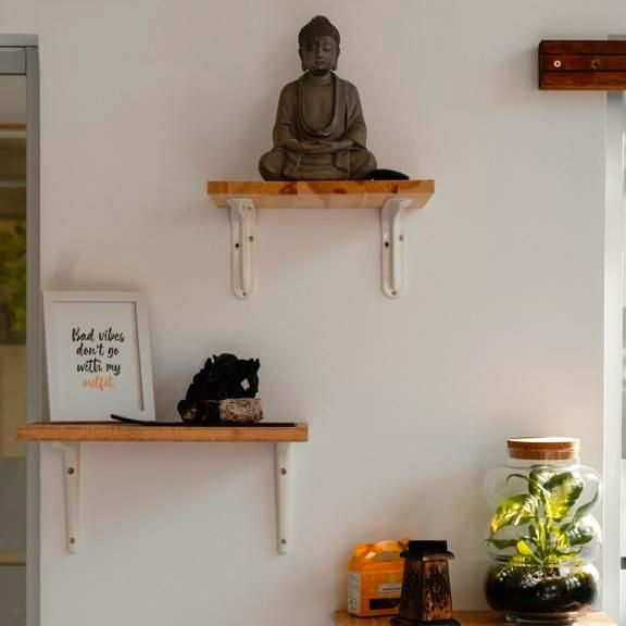 White wall with three wooden shelves holding a Buddha statue, plants, and decor.
