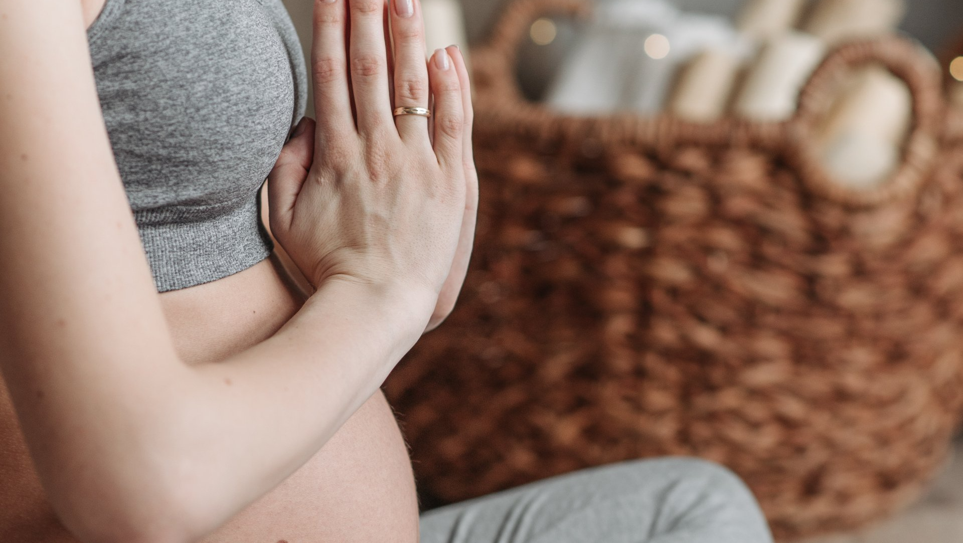 Pregnant person in gray athletic wear, hands together in prayer position. Wicker basket in background.