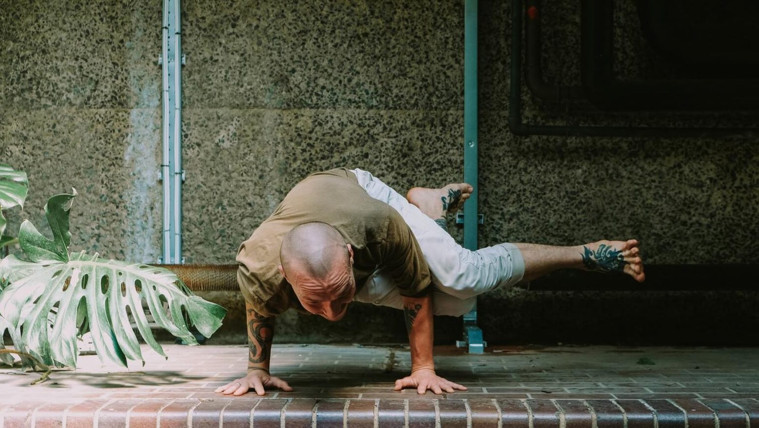 Man in yoga pose, balancing on hands with one leg extended, outdoors.