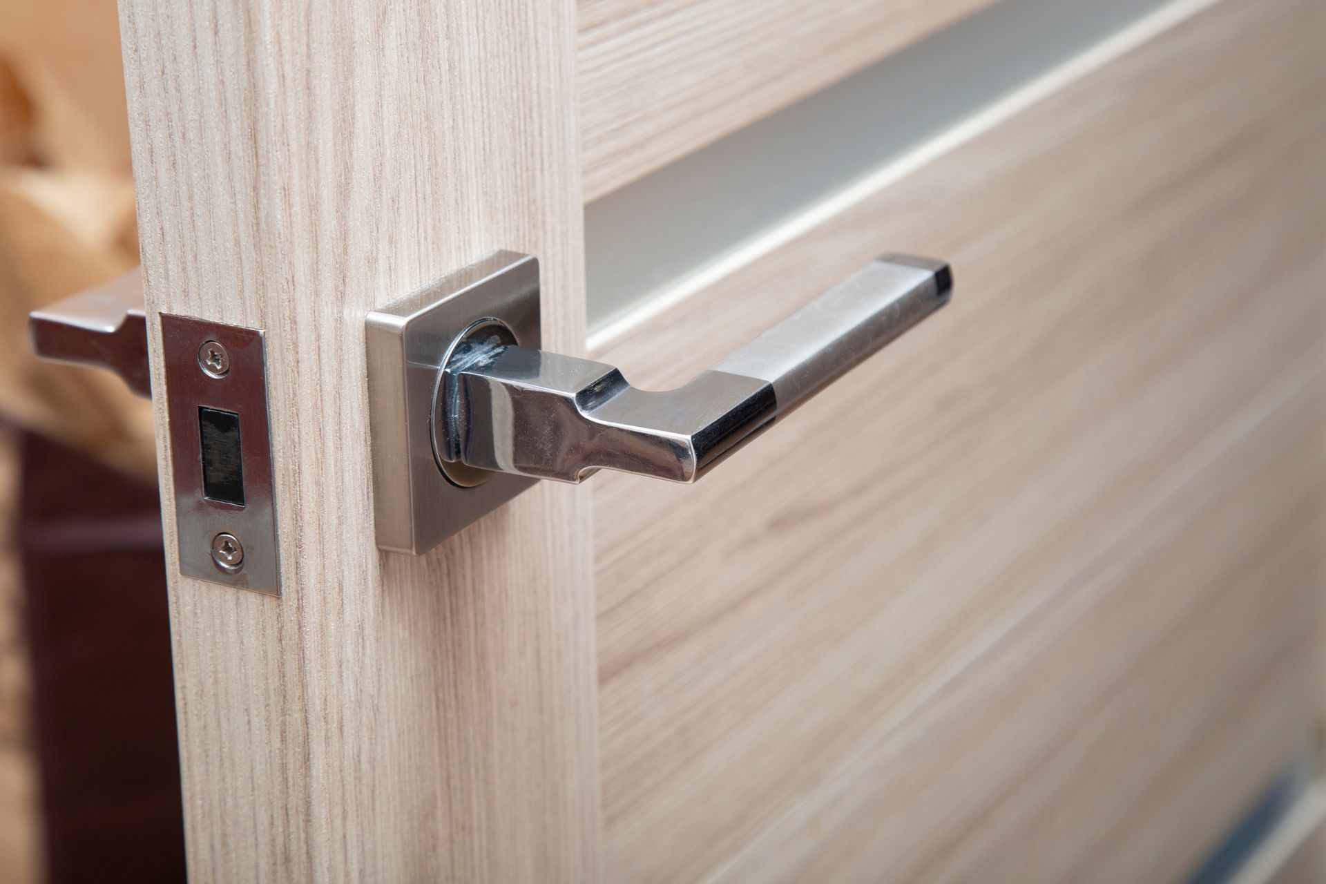 Close-up of a silver door handle on a light wood door with the latch plate visible.