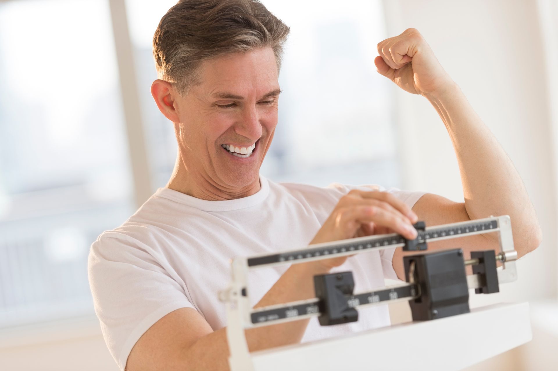 Man excitedly checks weight on scale, smiling and flexing arm.