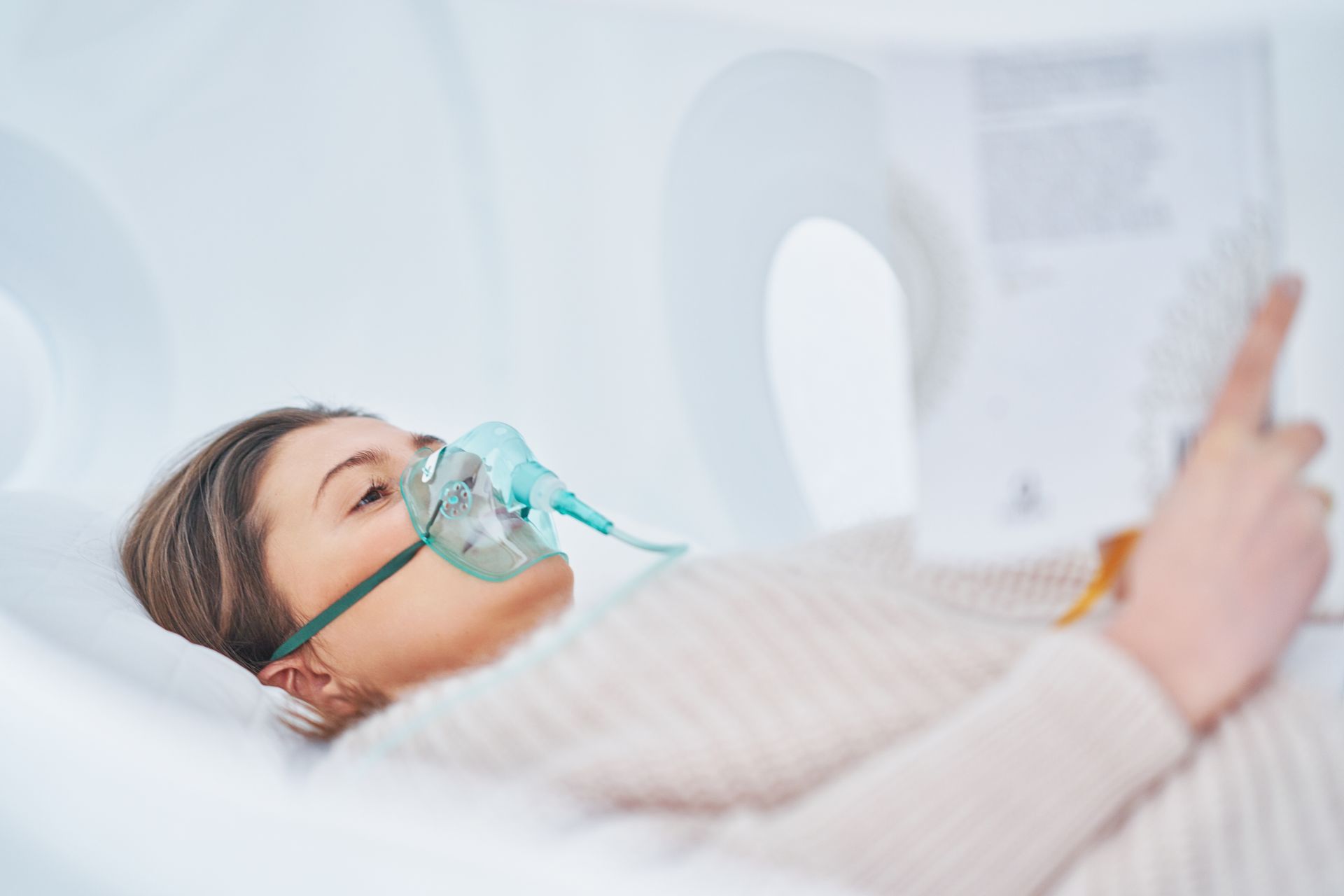 Woman with oxygen mask reading in a medical setting.