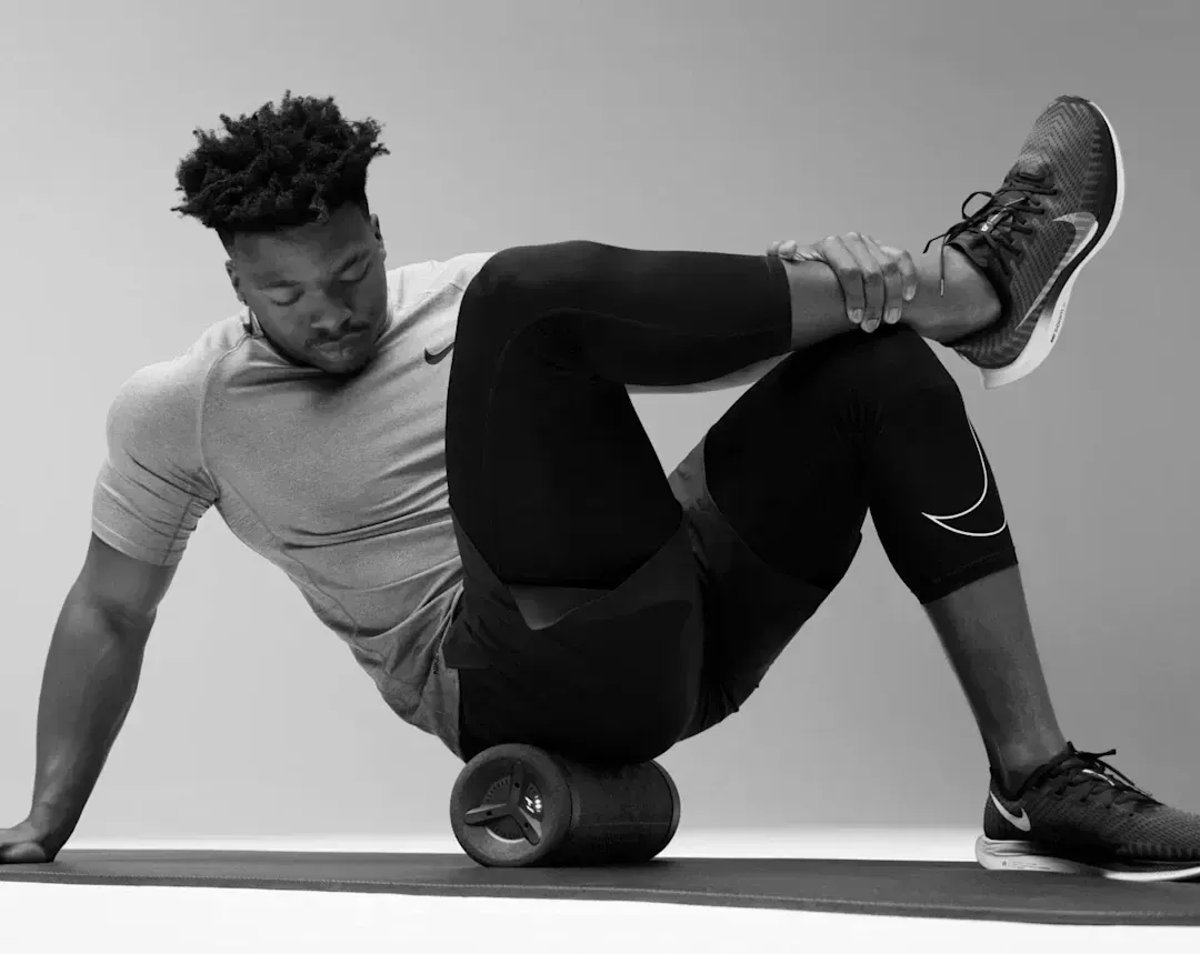 Man stretching on foam roller, lying on his side with leg crossed and hands on his thigh.