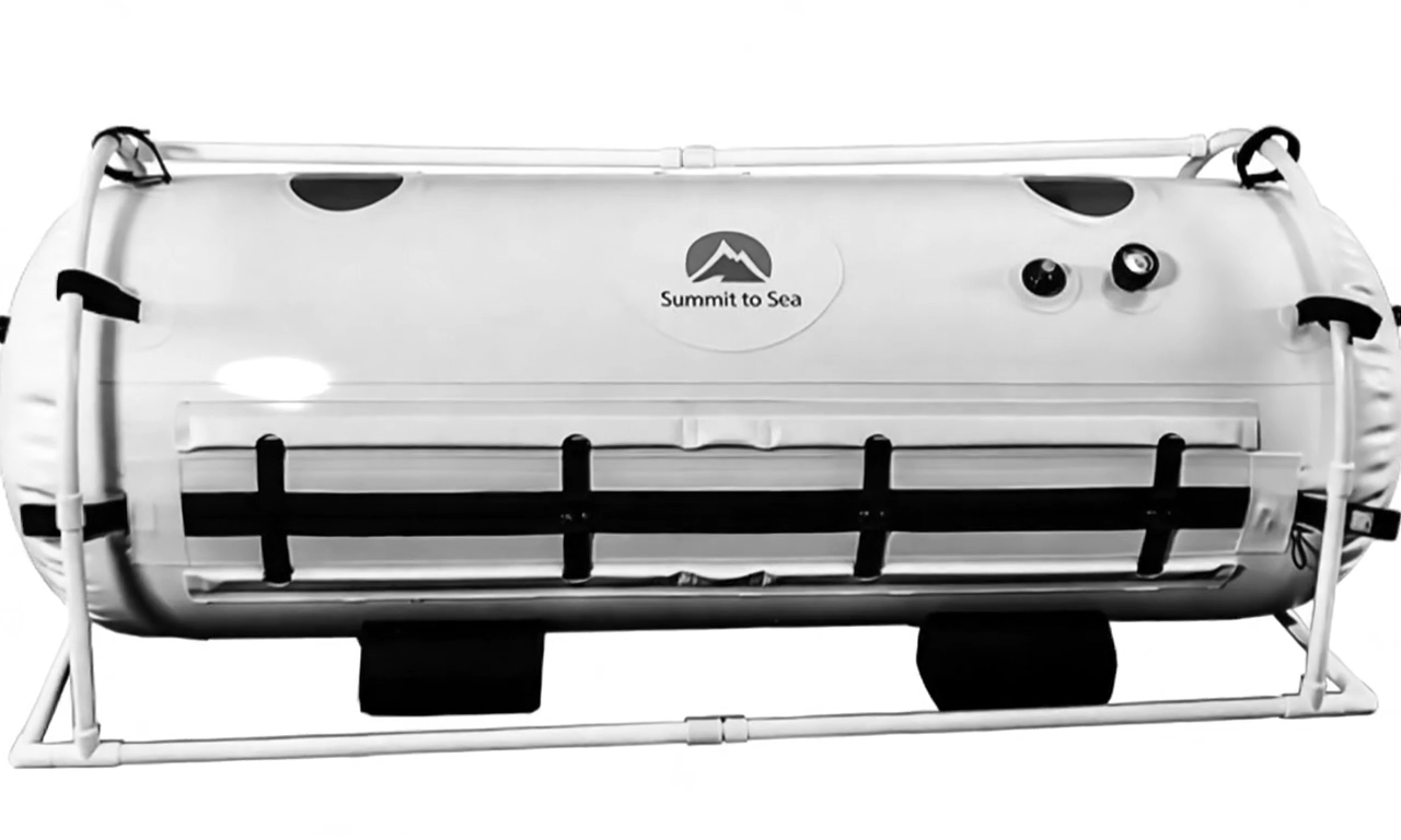 Hyperbaric oxygen chamber with Summit to Sea logo. Cylindrical, with restraints and control panel.