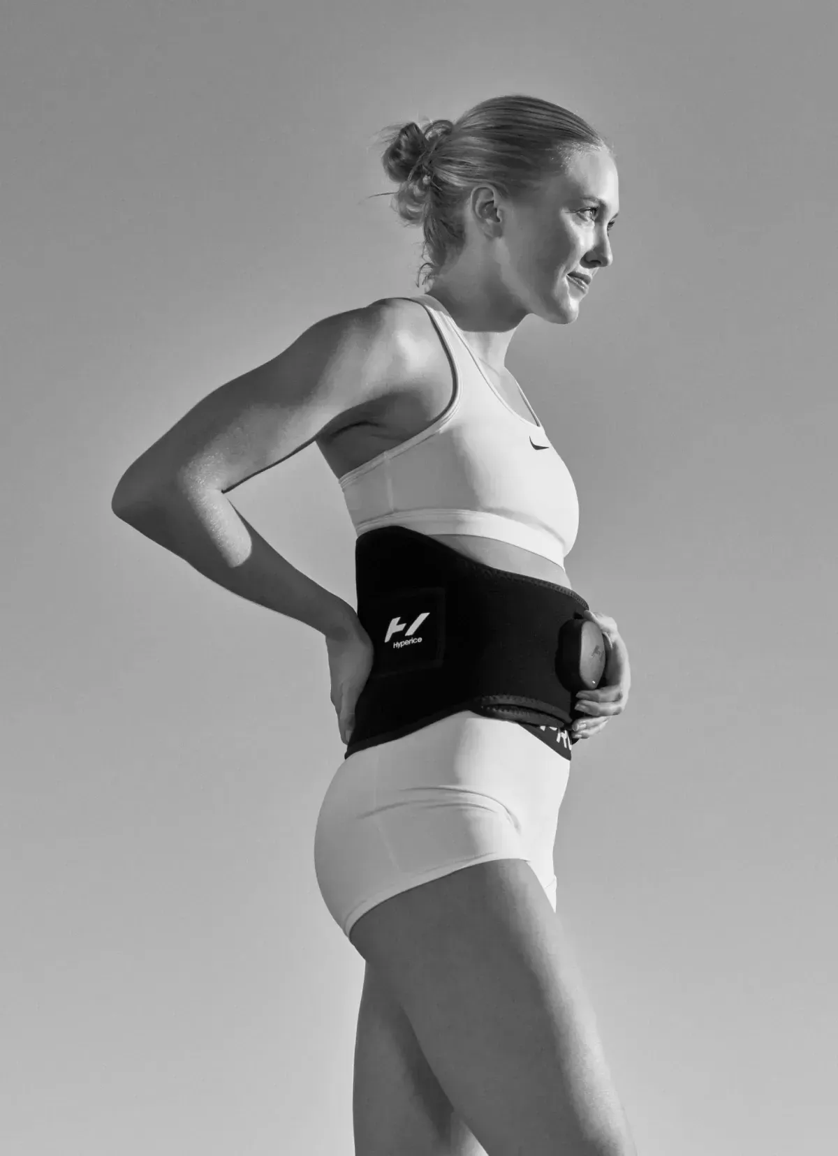 Woman wearing a black back brace, outdoors. She is wearing white athletic clothes and is looking to the side.
