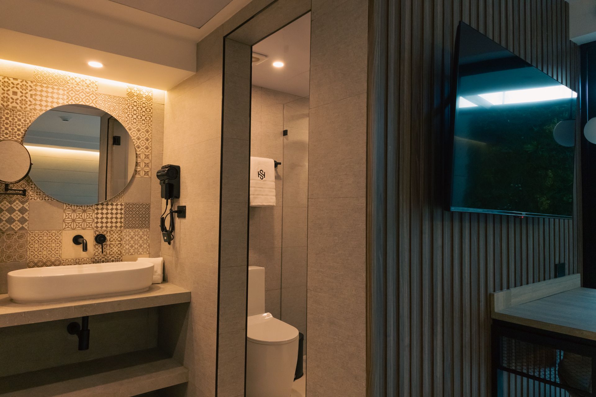 A bathroom with a sink , toilet , mirror and television.