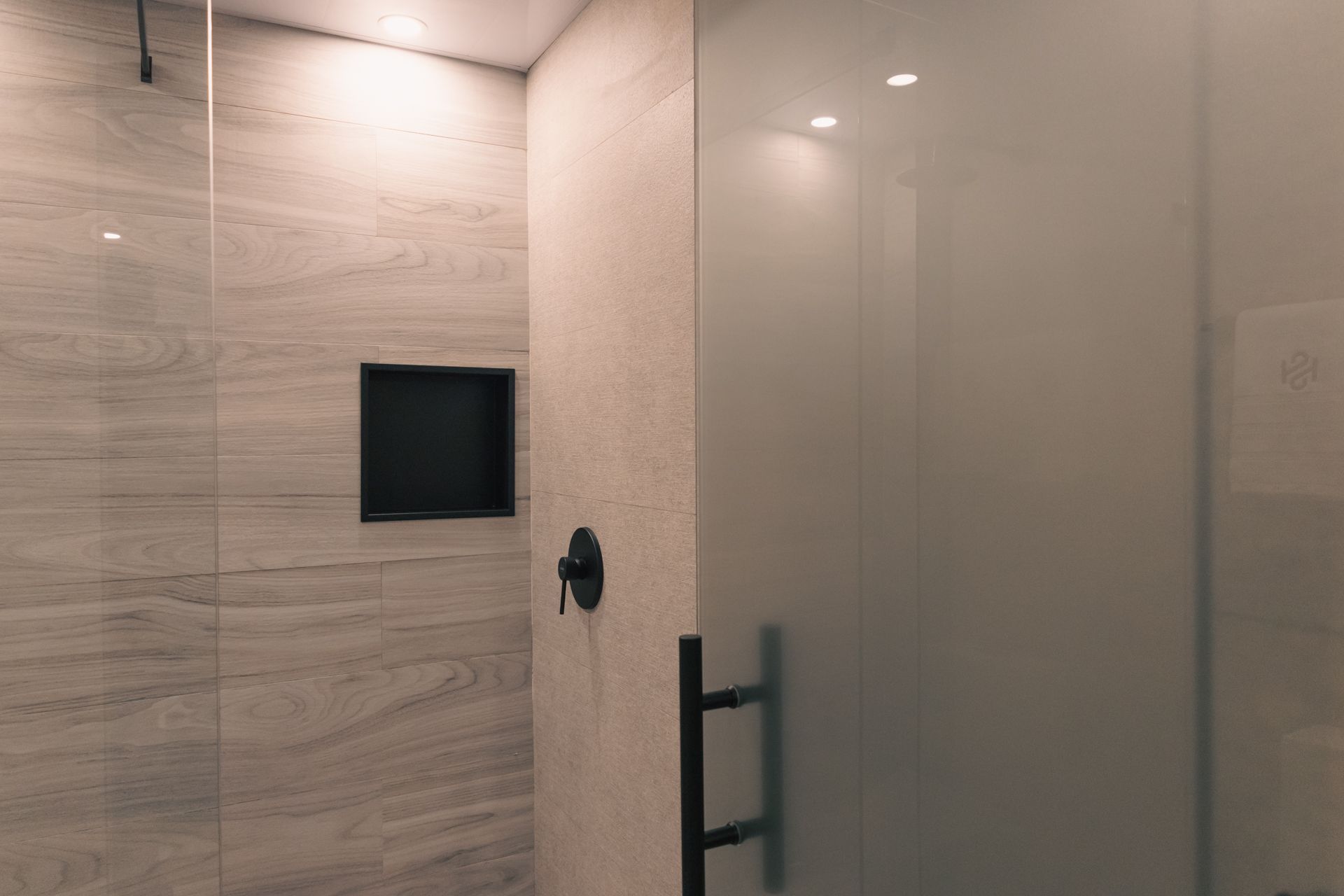 A bathroom with a glass shower door and a black handle.