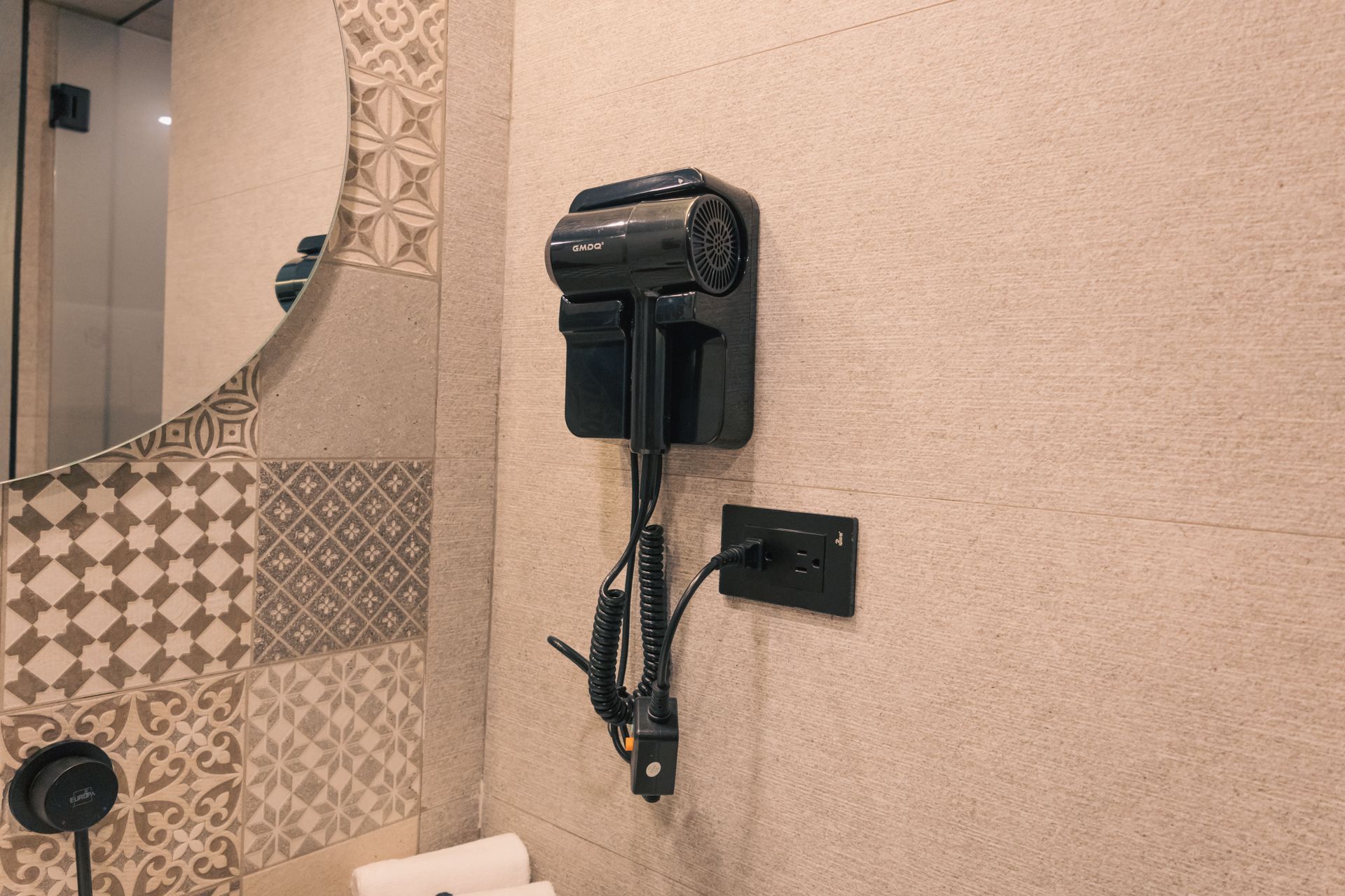 A hair dryer is hanging on a wall in a bathroom next to a mirror.