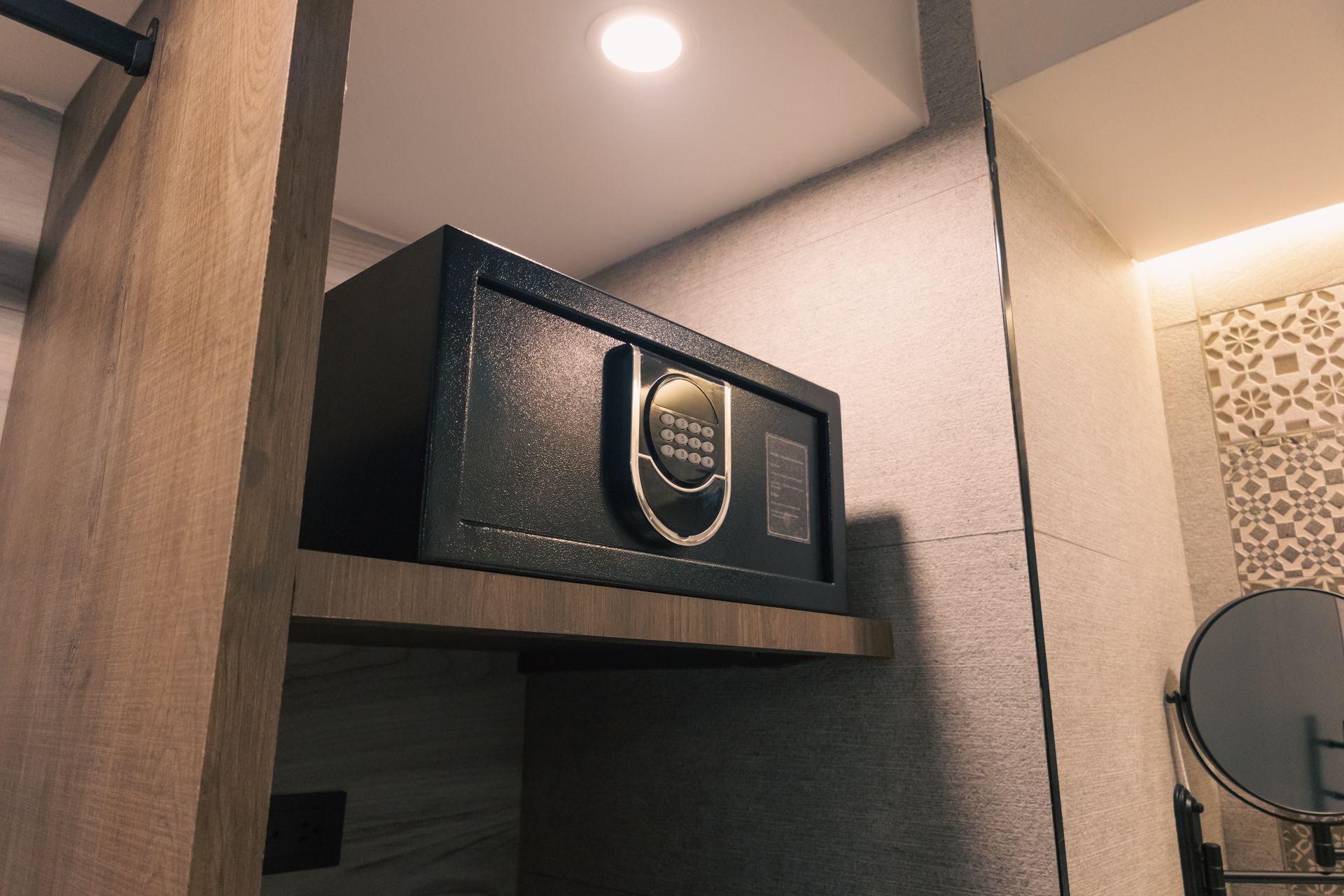 A safe is sitting on top of a wooden shelf in a bathroom next to a mirror.