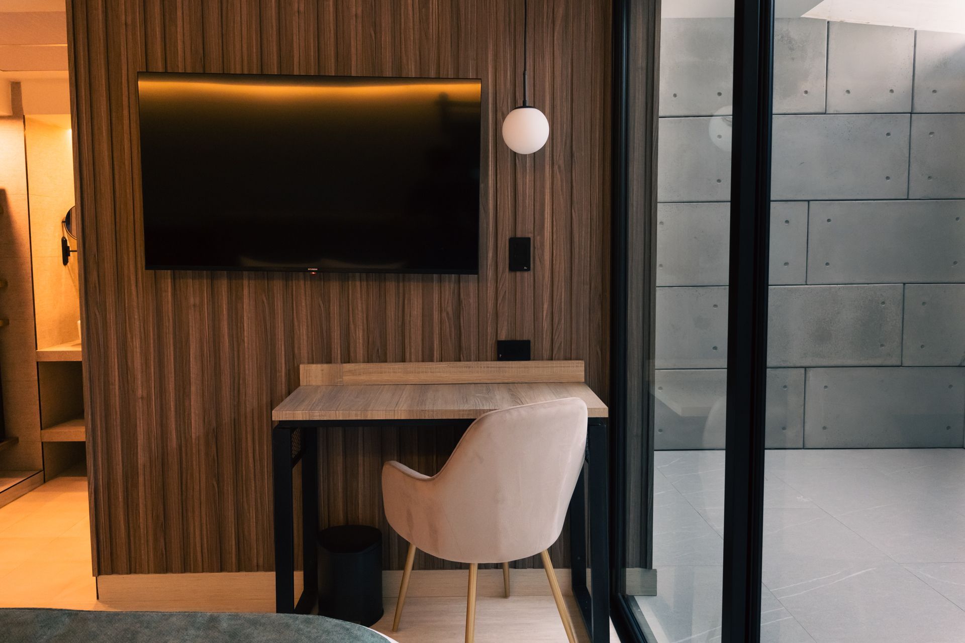 A hotel room with a desk , chair , television and a large window.