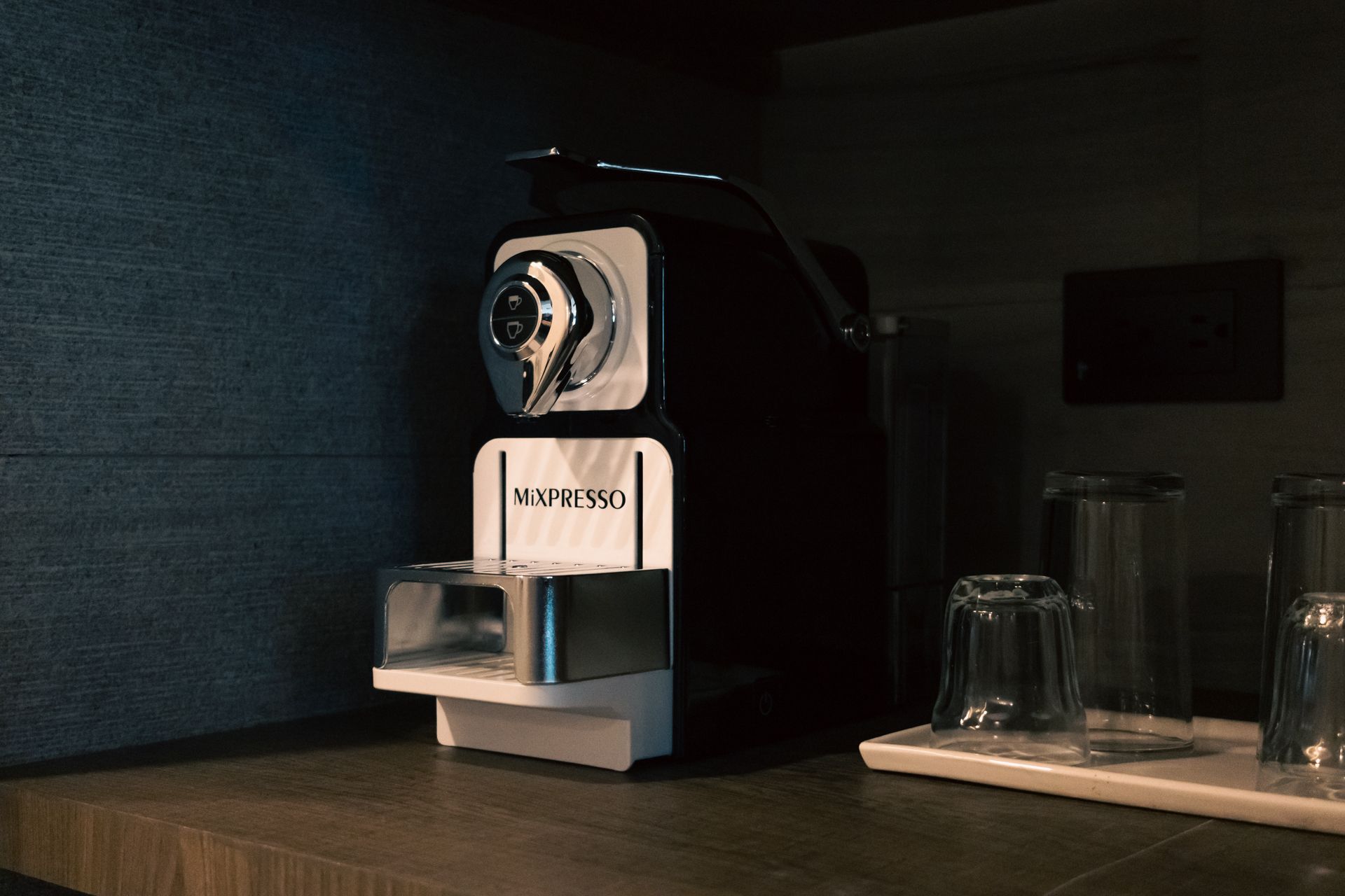 A nespresso coffee maker is sitting on a counter next to glasses.