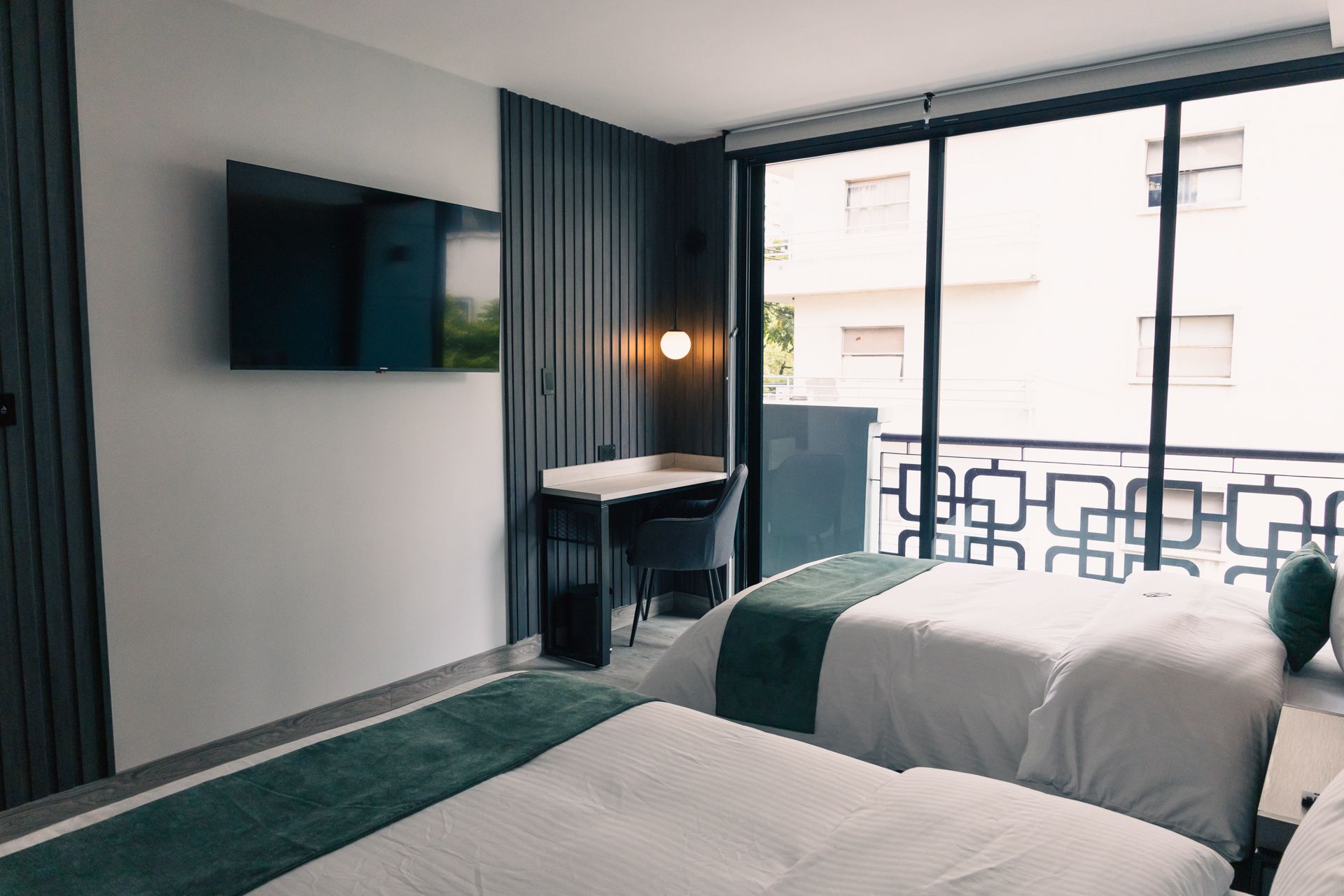A hotel room with two beds , a desk , a flat screen tv and a balcony.