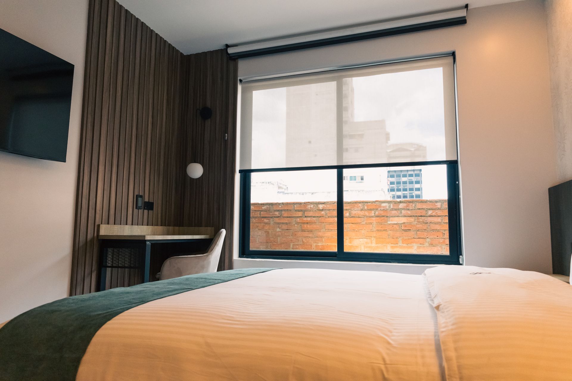 A hotel room with a bed , desk , television and large window.