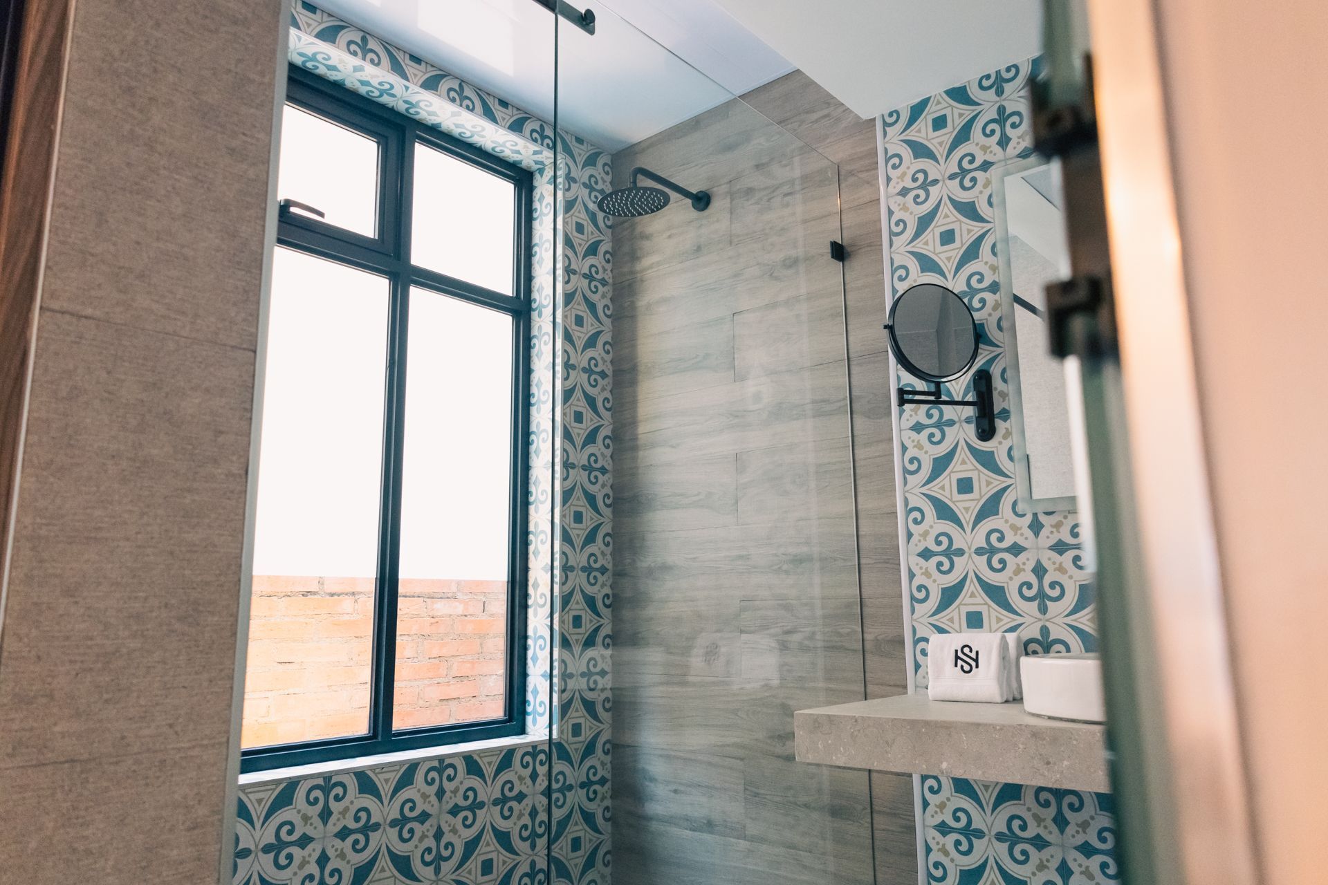 A bathroom with a shower , sink , mirror and window.