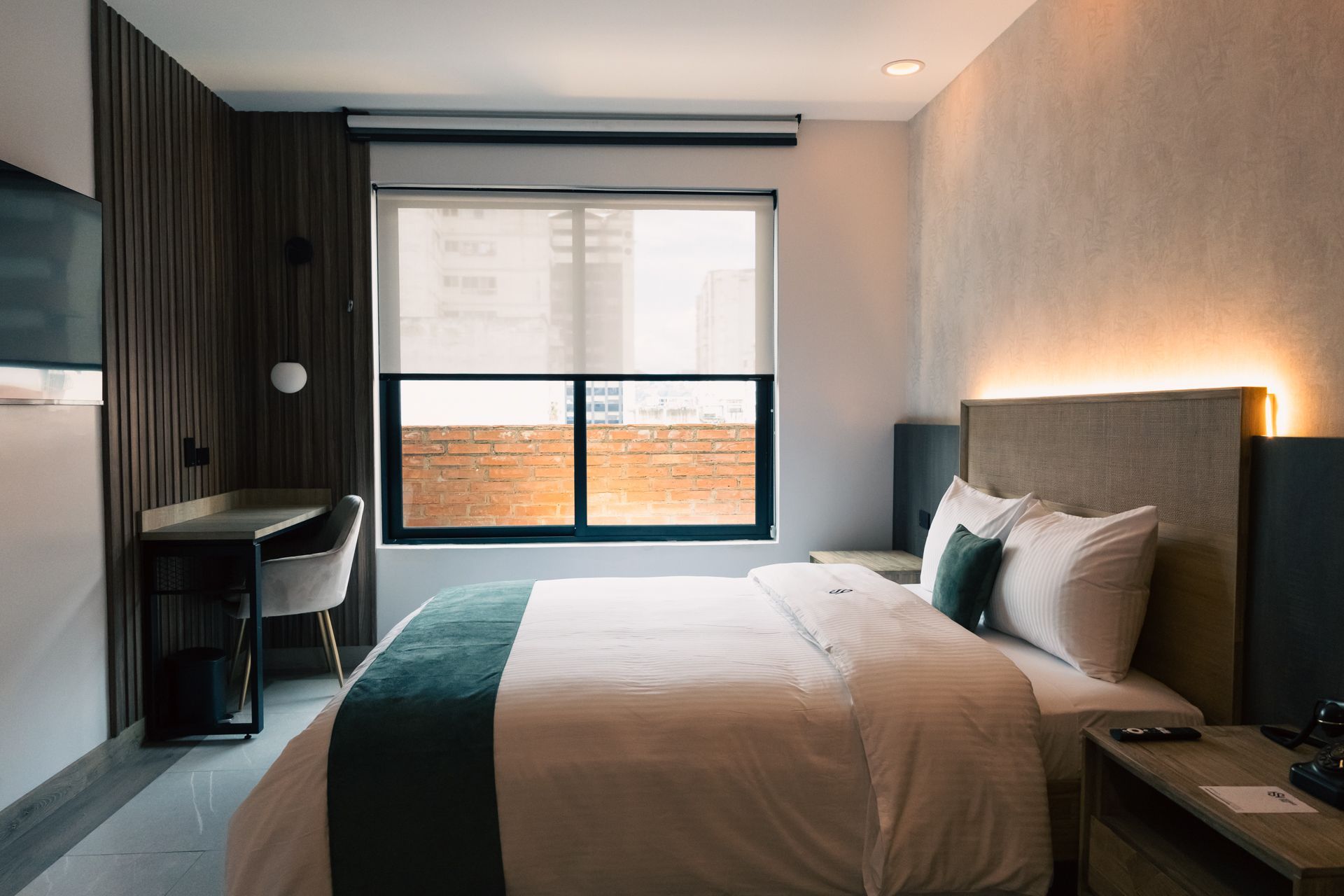 A hotel room with a bed , desk , television and window.