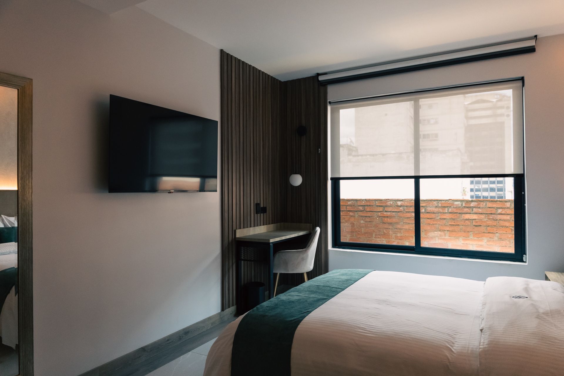 A hotel room with a bed , desk , television and window.
