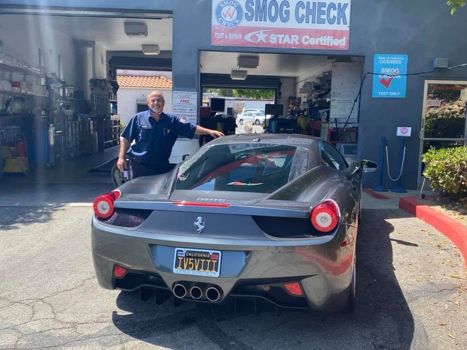 Black Ferrari parked at a smog check shop with a man standing beside it