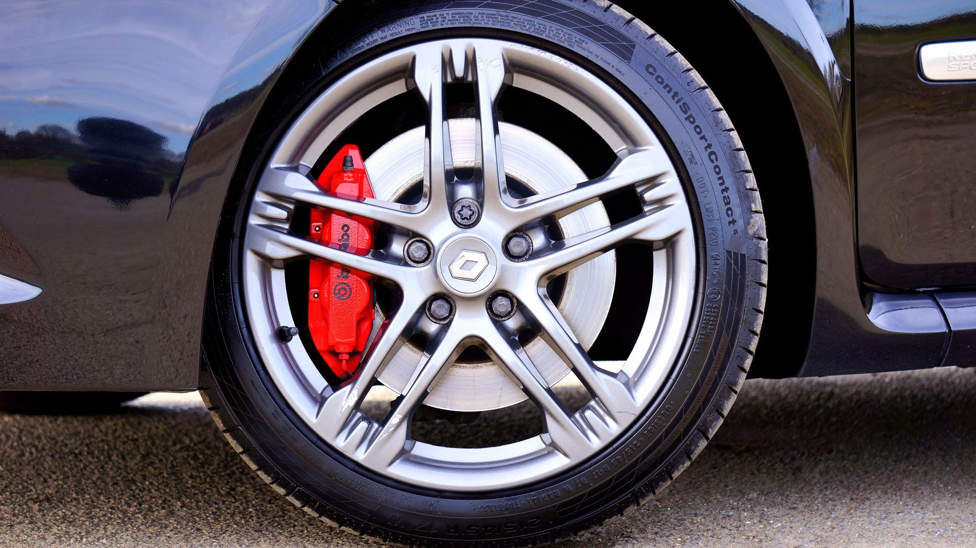 Close-up of a car wheel with silver alloy rim and red brake caliper on a dark vehicle
