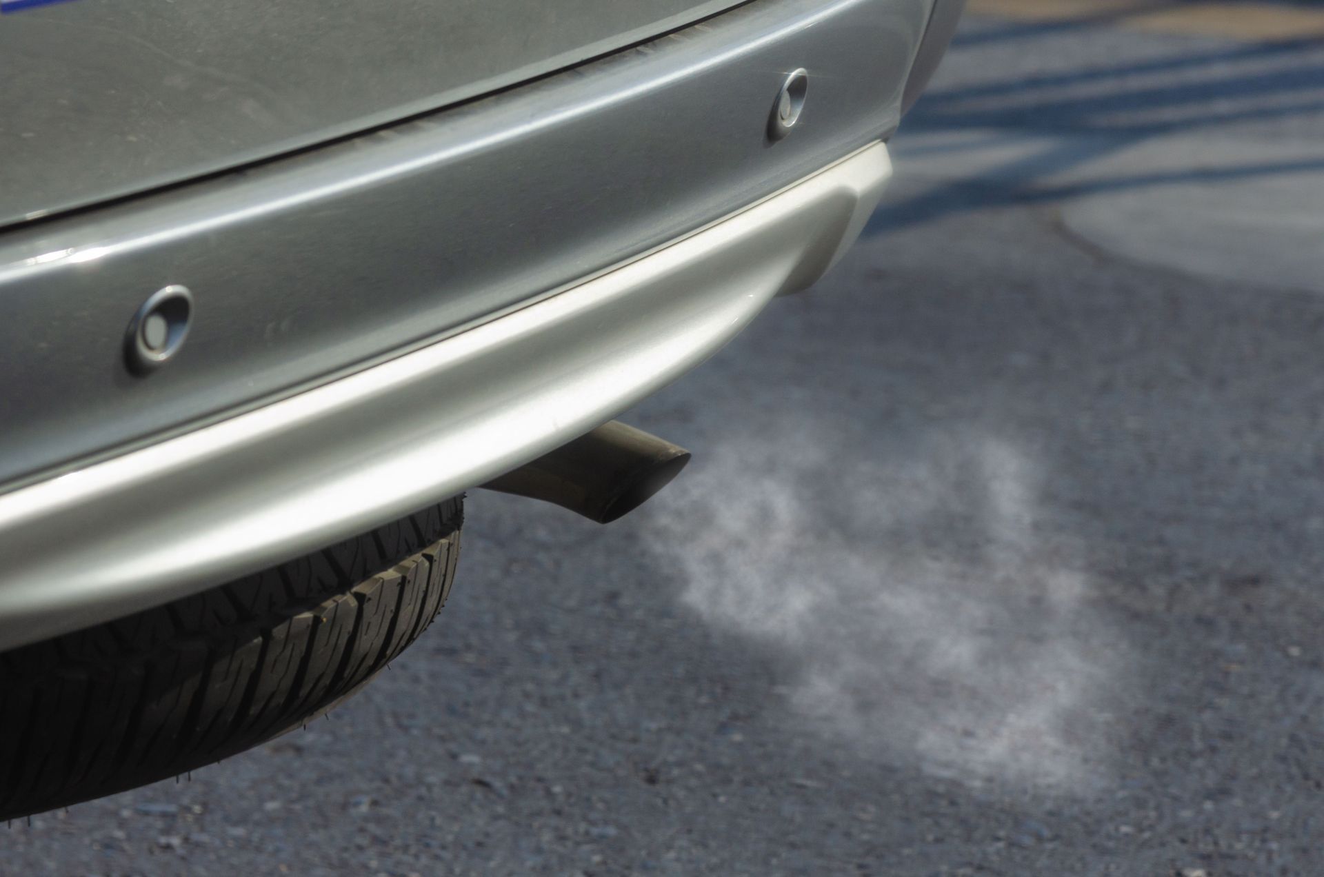 Car exhaust pipe releasing white smoke beside the rear tire on a road