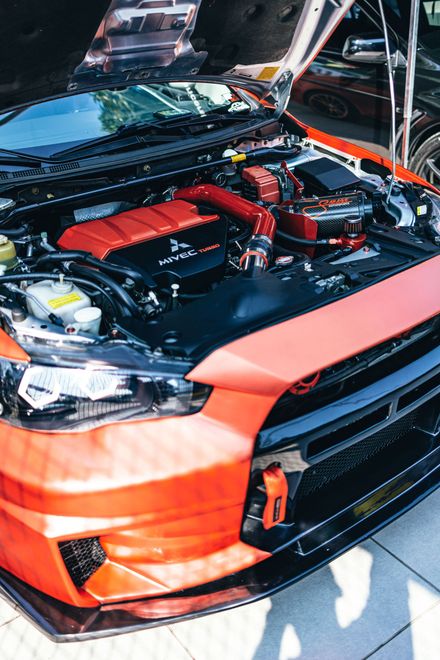 Orange sports car with hood open, showing a modified engine bay with red components