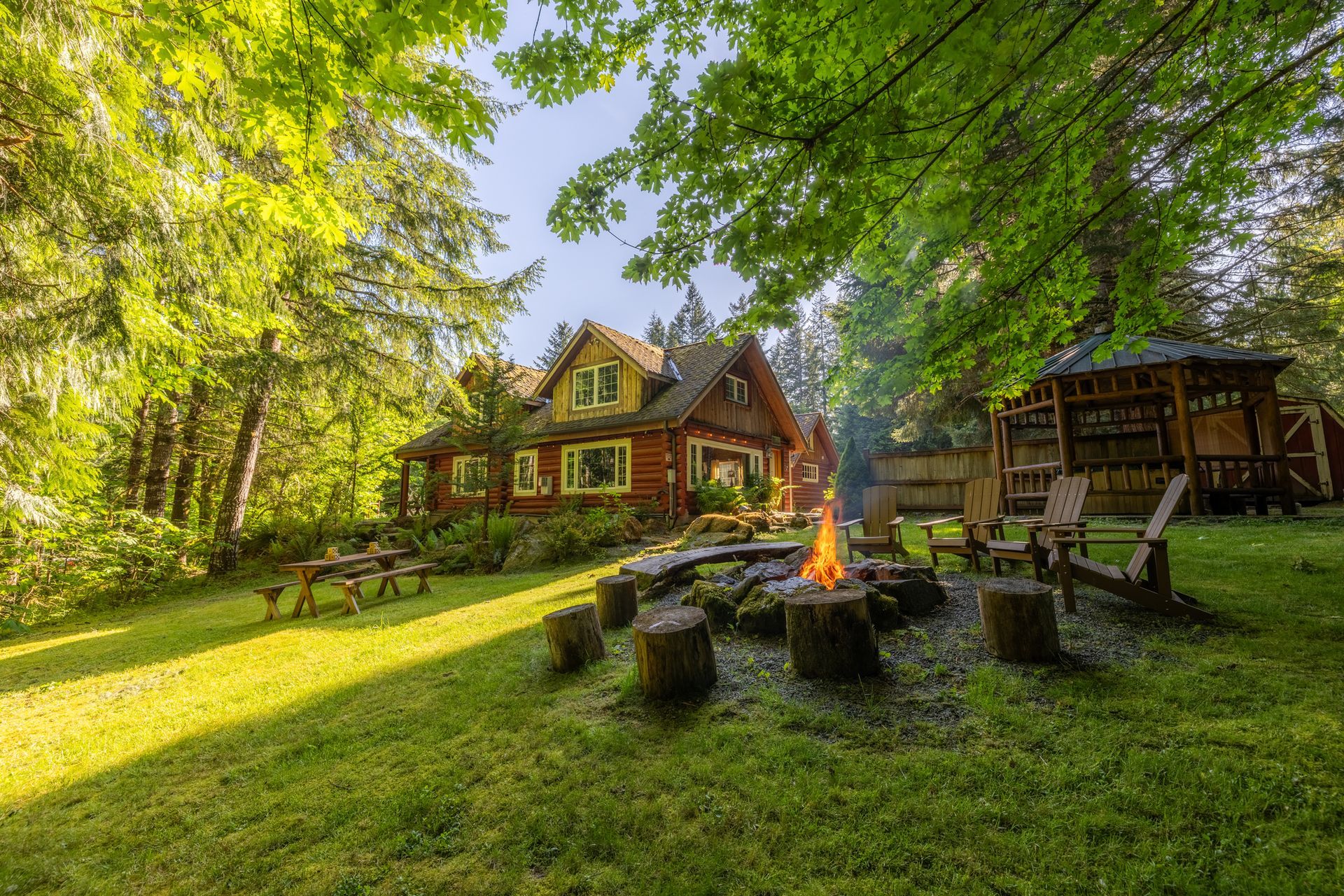 A log cabin in the middle of a forest with a picnic table in front of it.