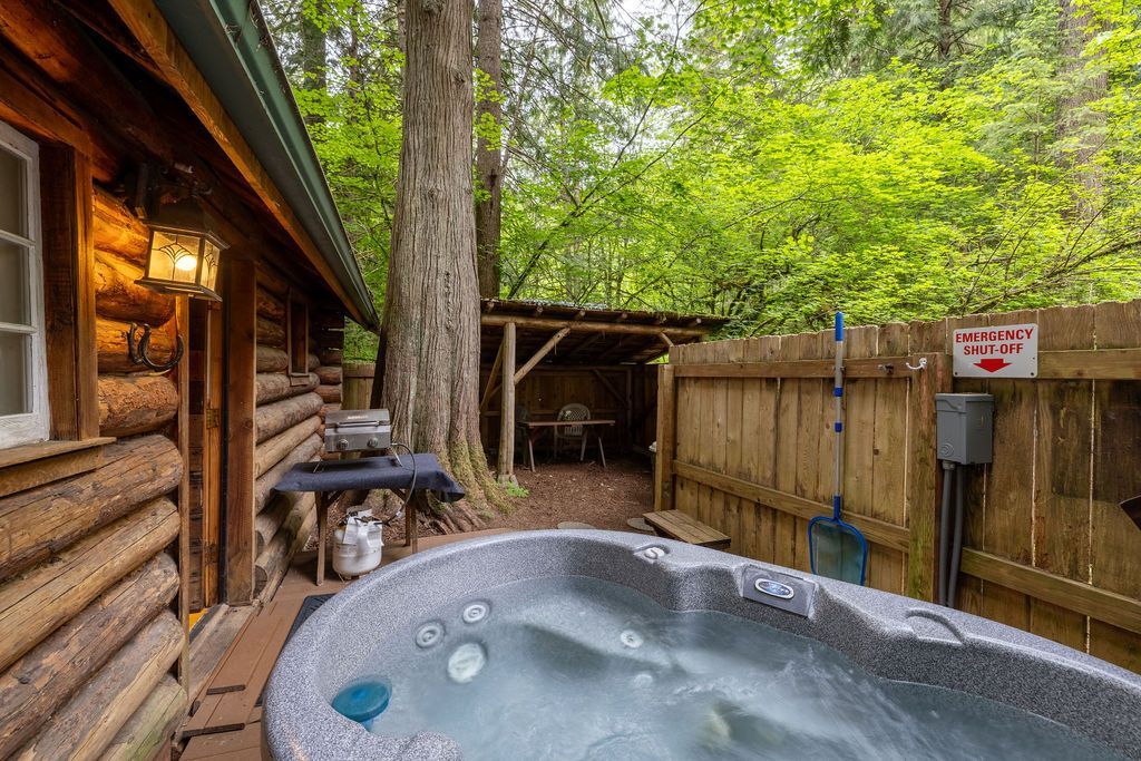 A rustic log cabin with a hot tub in an outdoor enclosure, surrounded by trees.