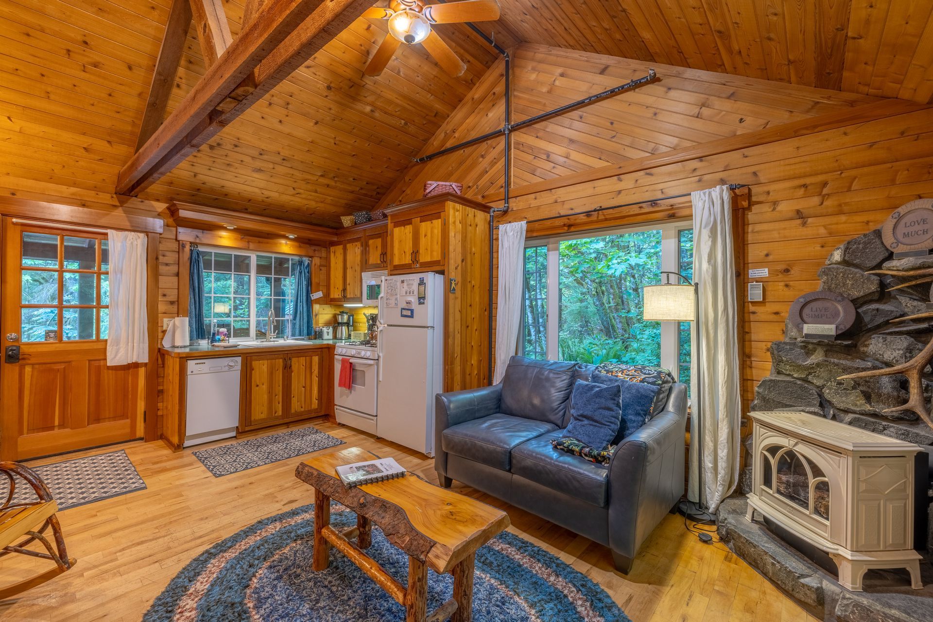 Cozy cabin interior with wooden walls, a blue couch, fireplace, and a small kitchen area.