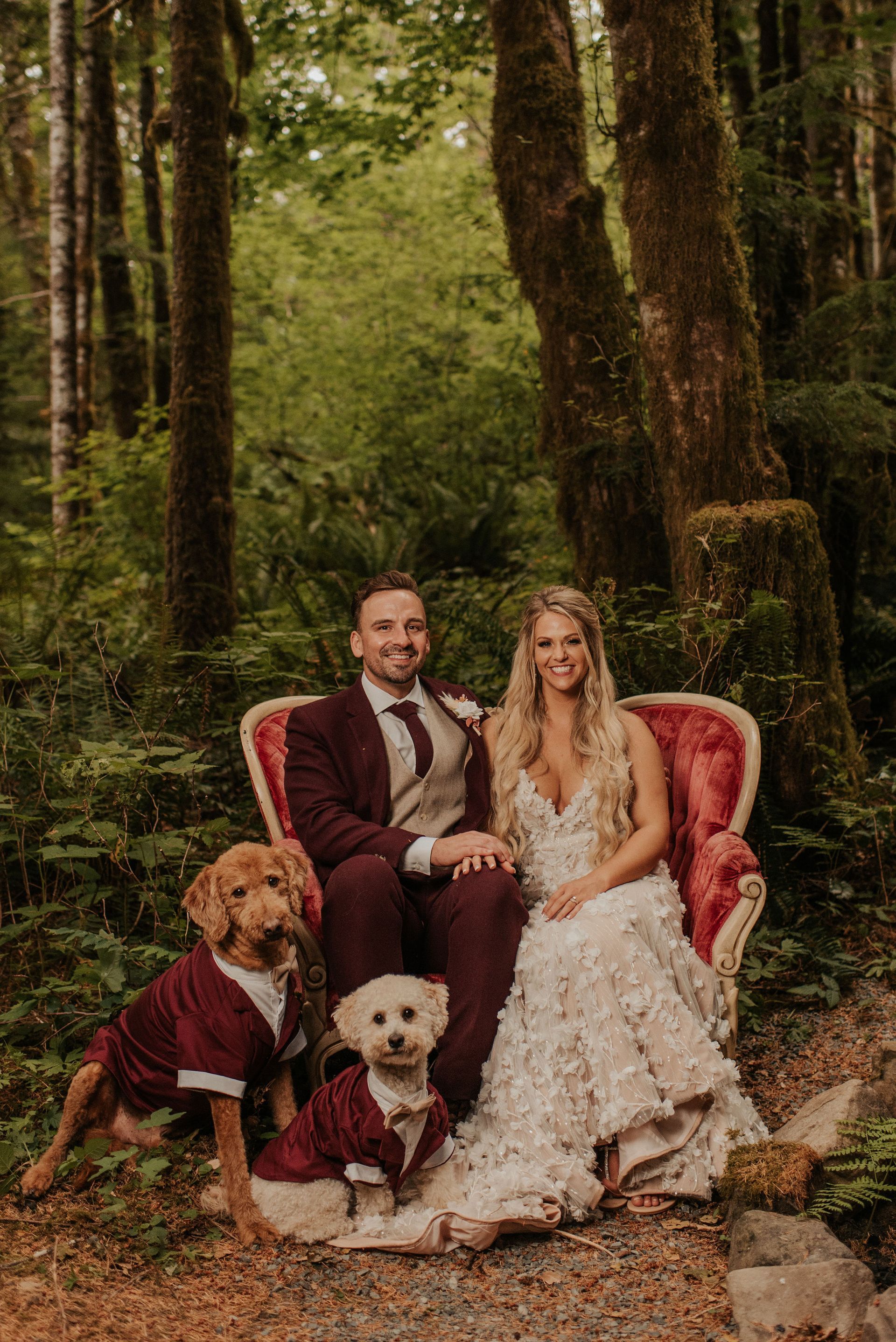 A bride and groom are posing for a picture with their dogs in the woods.