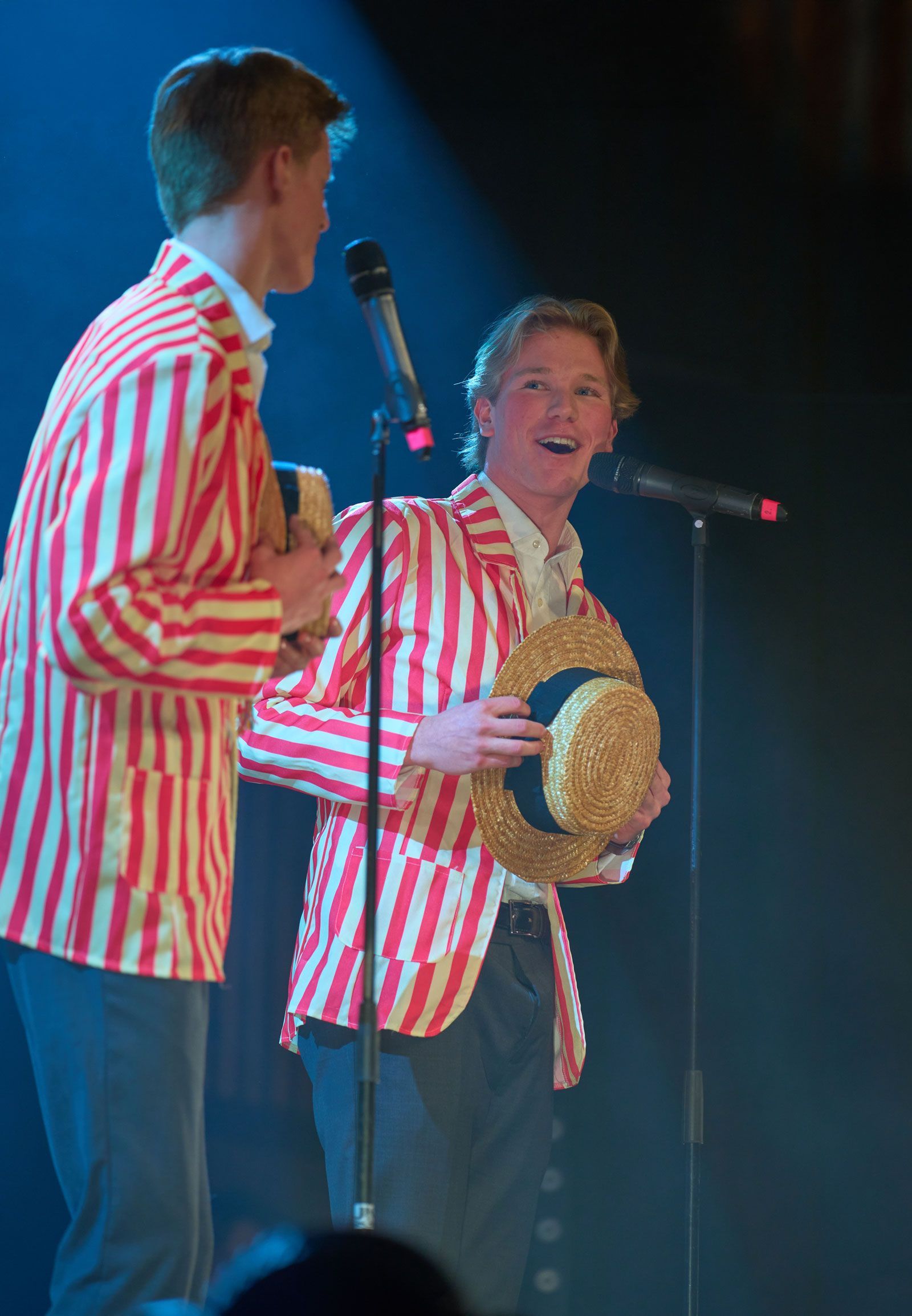 Två artister i rödvitrandiga jackor på scenen, en håller en stråhatt och ler mot en mikrofon