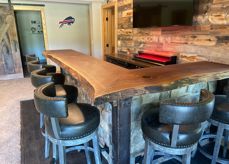 A bar with stools and a wooden table in a room with a buffalo bills logo on the wall.