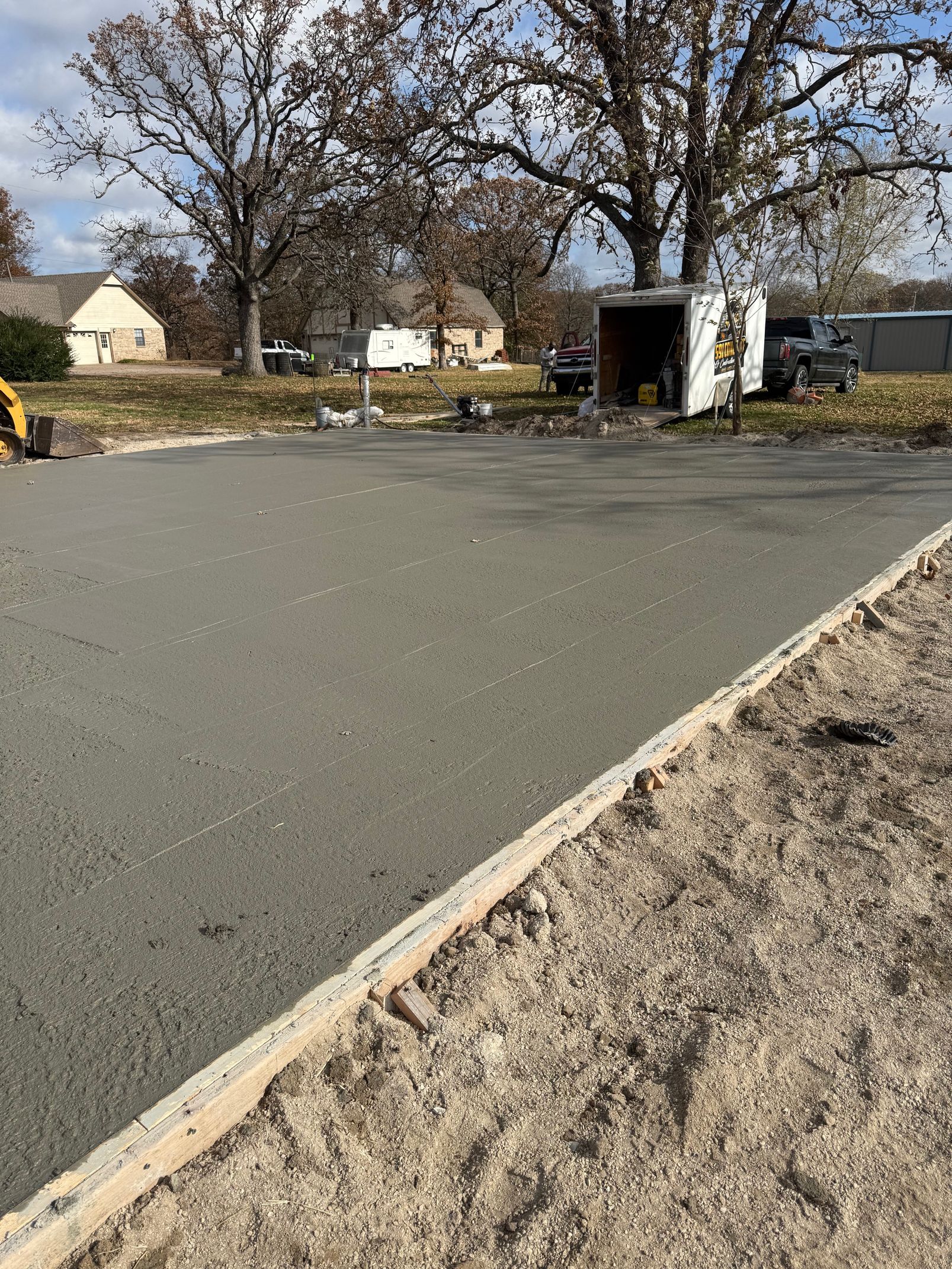 Newly poured concrete slab with wooden formwork, in a residential setting.