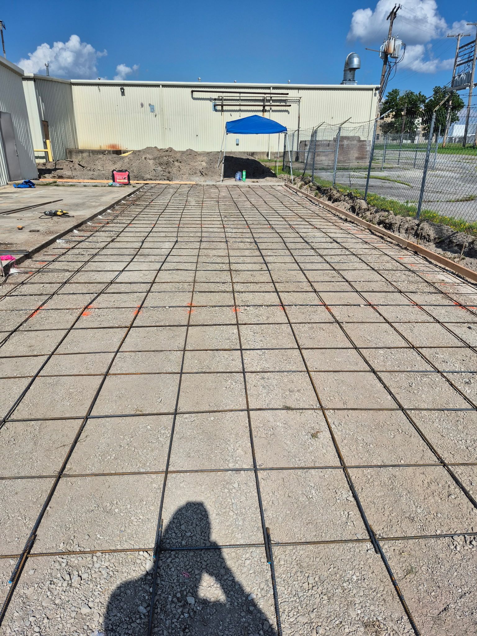 Outdoor paved courtyard with a grid of bricks, a blue canopy, and a cream building wall under a clear sky.