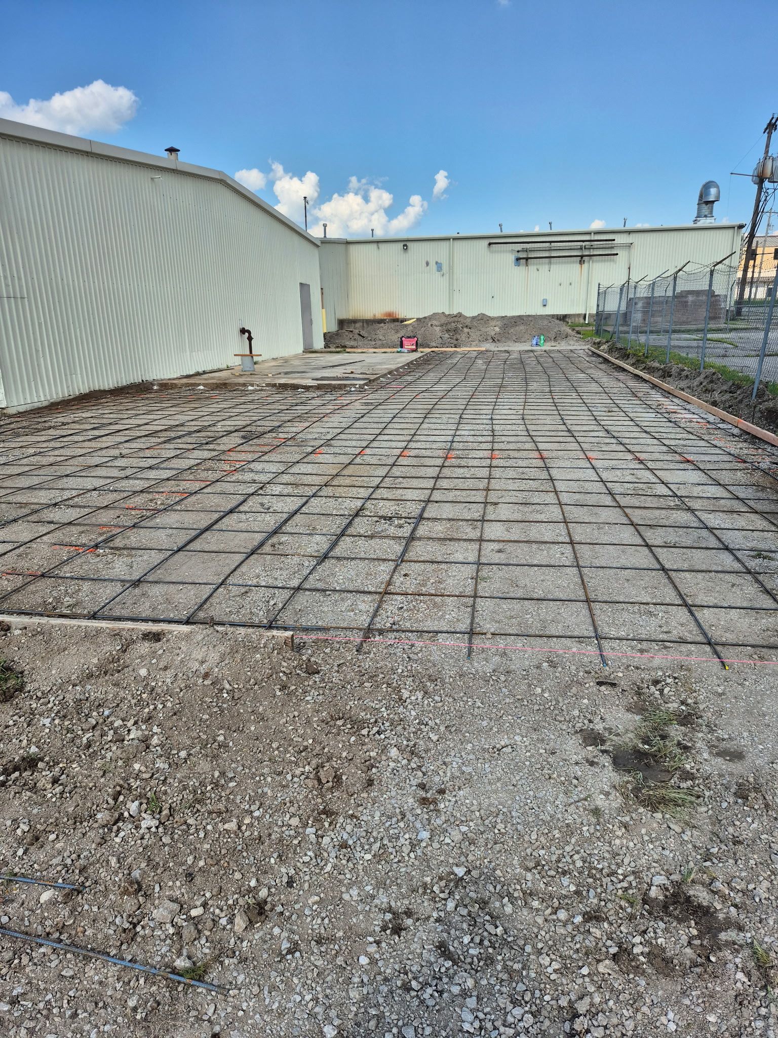Empty industrial rooftop with gravel, concrete pavers, and a pale blue wall under a partly cloudy sky