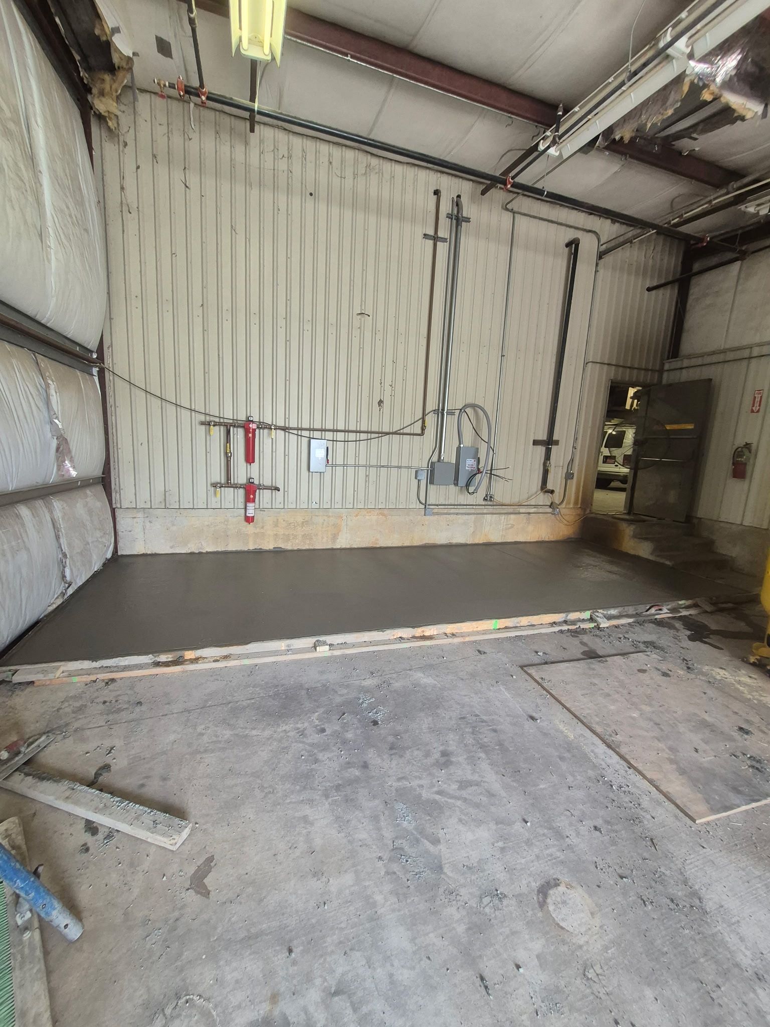 Empty industrial garage with concrete floor, corrugated metal walls, and a raised work platform against the back wall