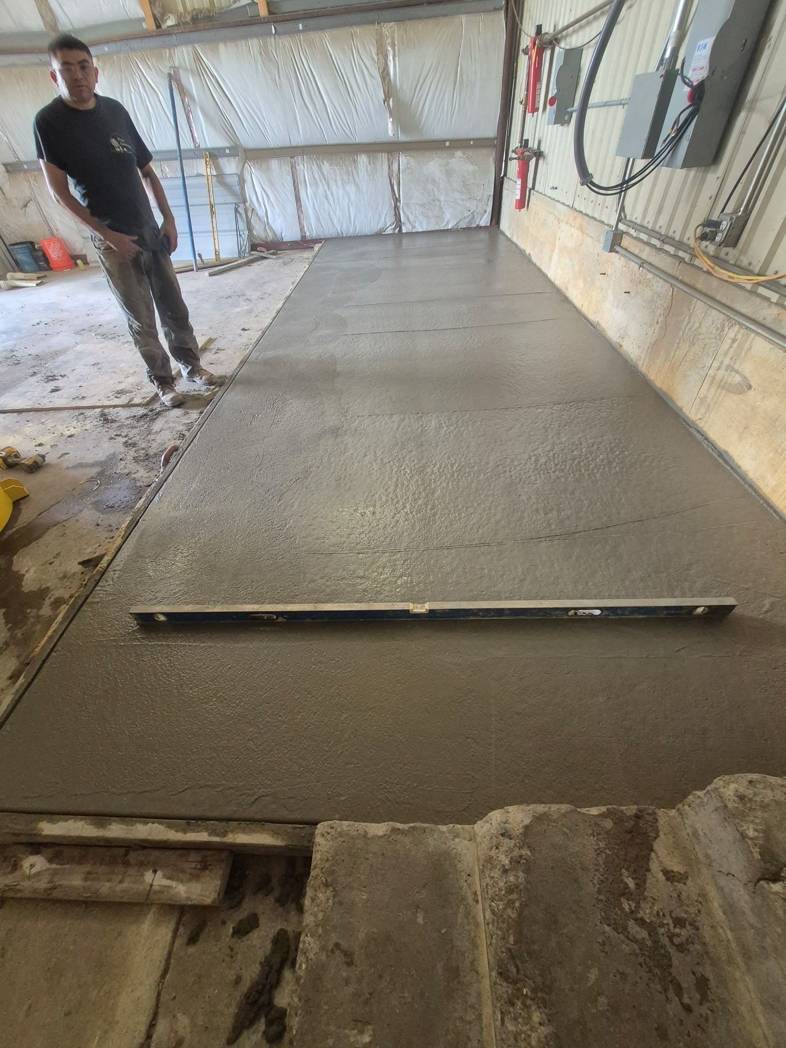 Fresh concrete slab being smoothed inside a garage, with a worker standing nearby.
