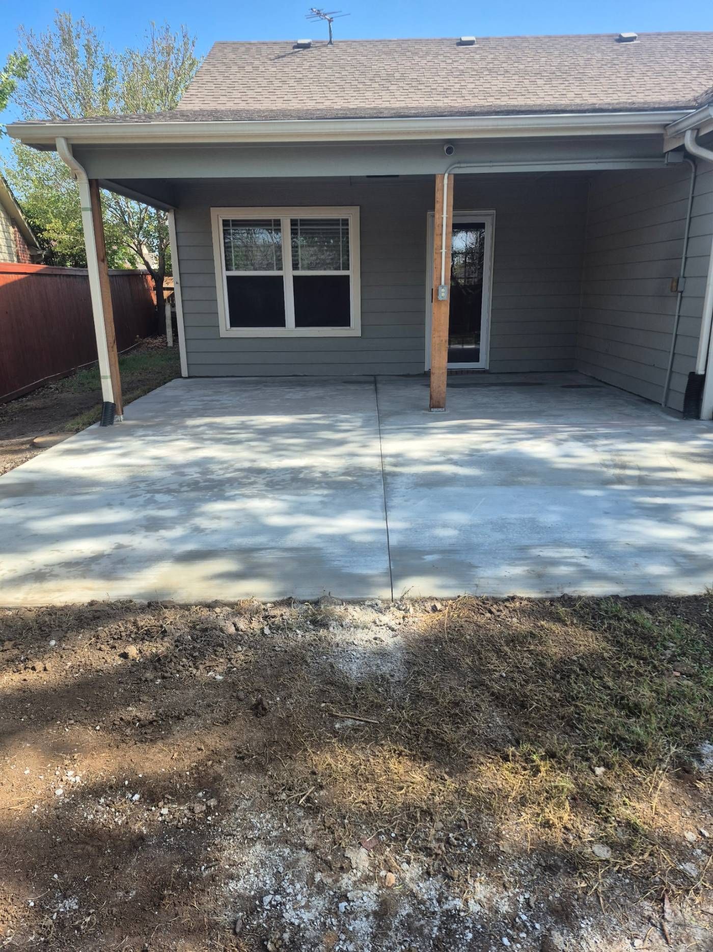 Concrete front patio with a gray house, white-trimmed windows, and a small porch roof.