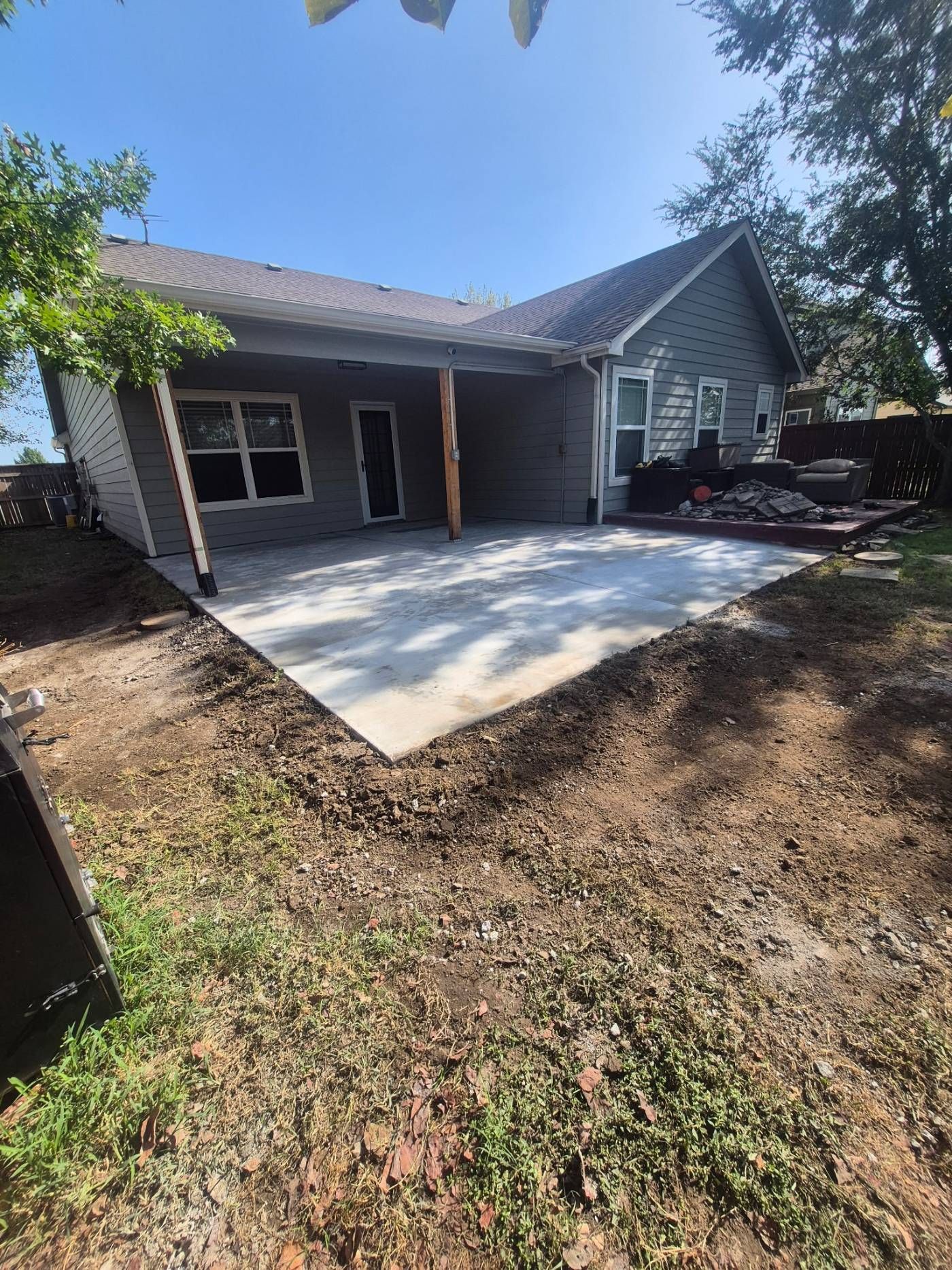 Back patio with fresh concrete slab beside a gray house and wooded yard