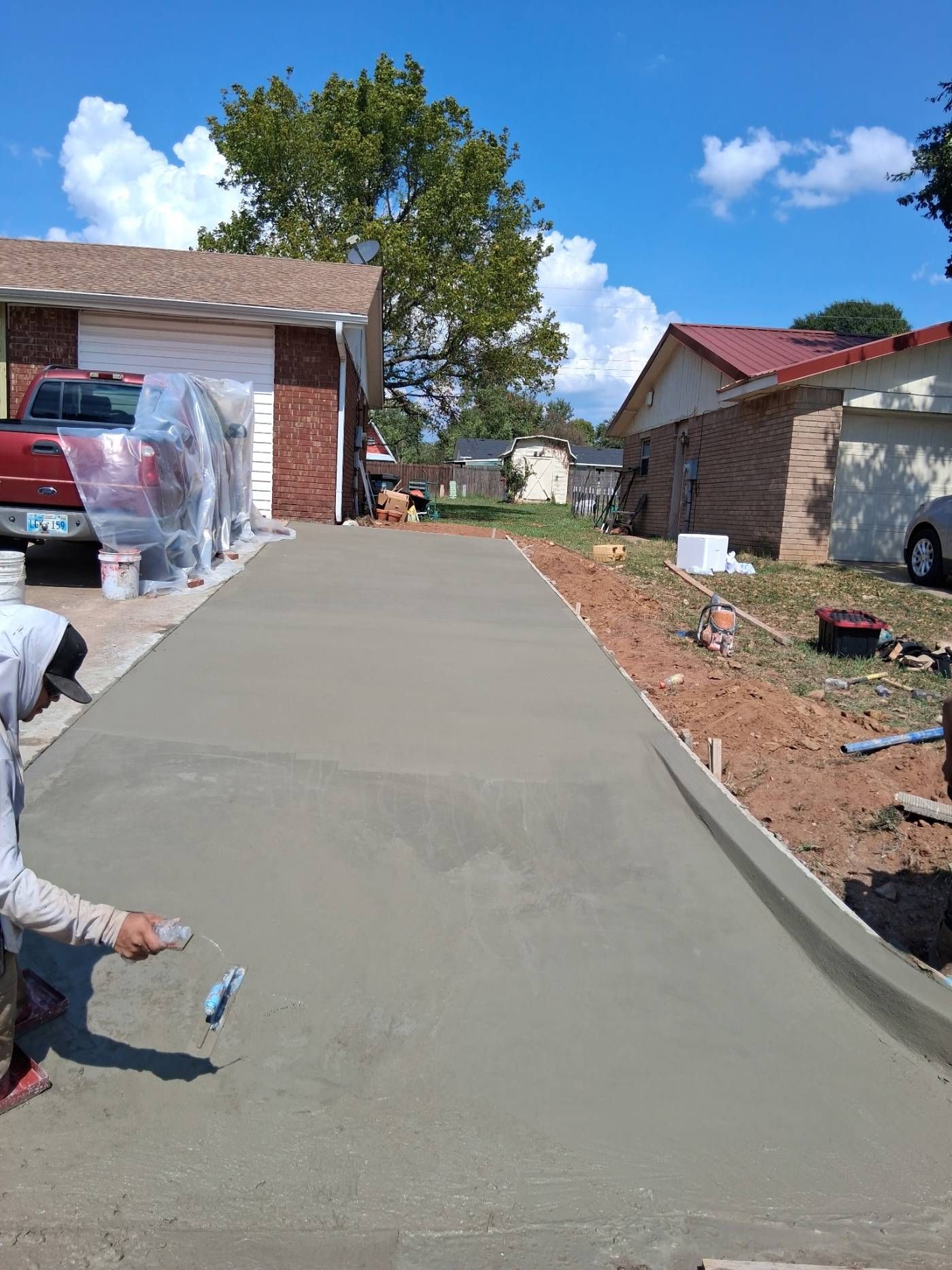 Freshly poured concrete driveway leading between houses, with a worker smoothing the surface.