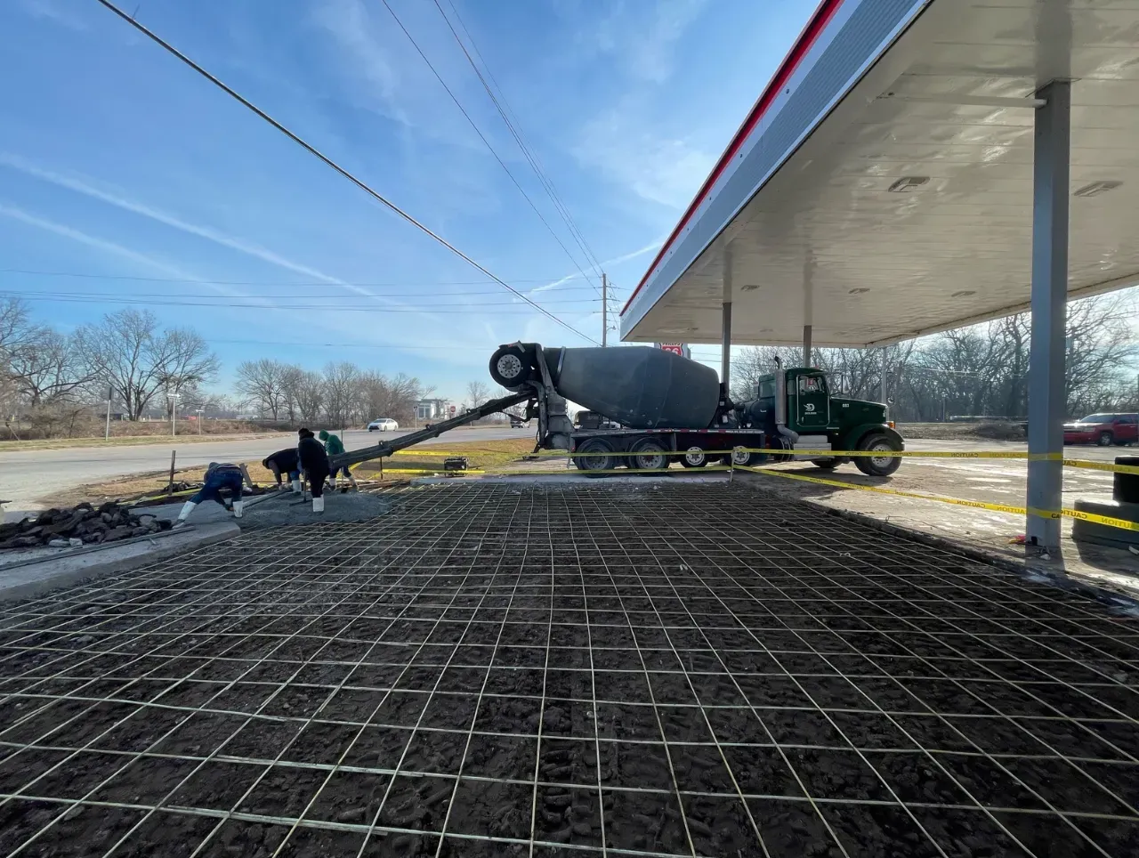 Concrete truck pouring concrete over rebar grid at gas station.