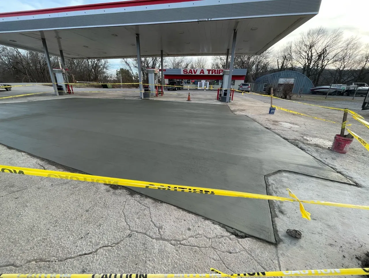 Newly poured concrete at a gas station with yellow caution tape.