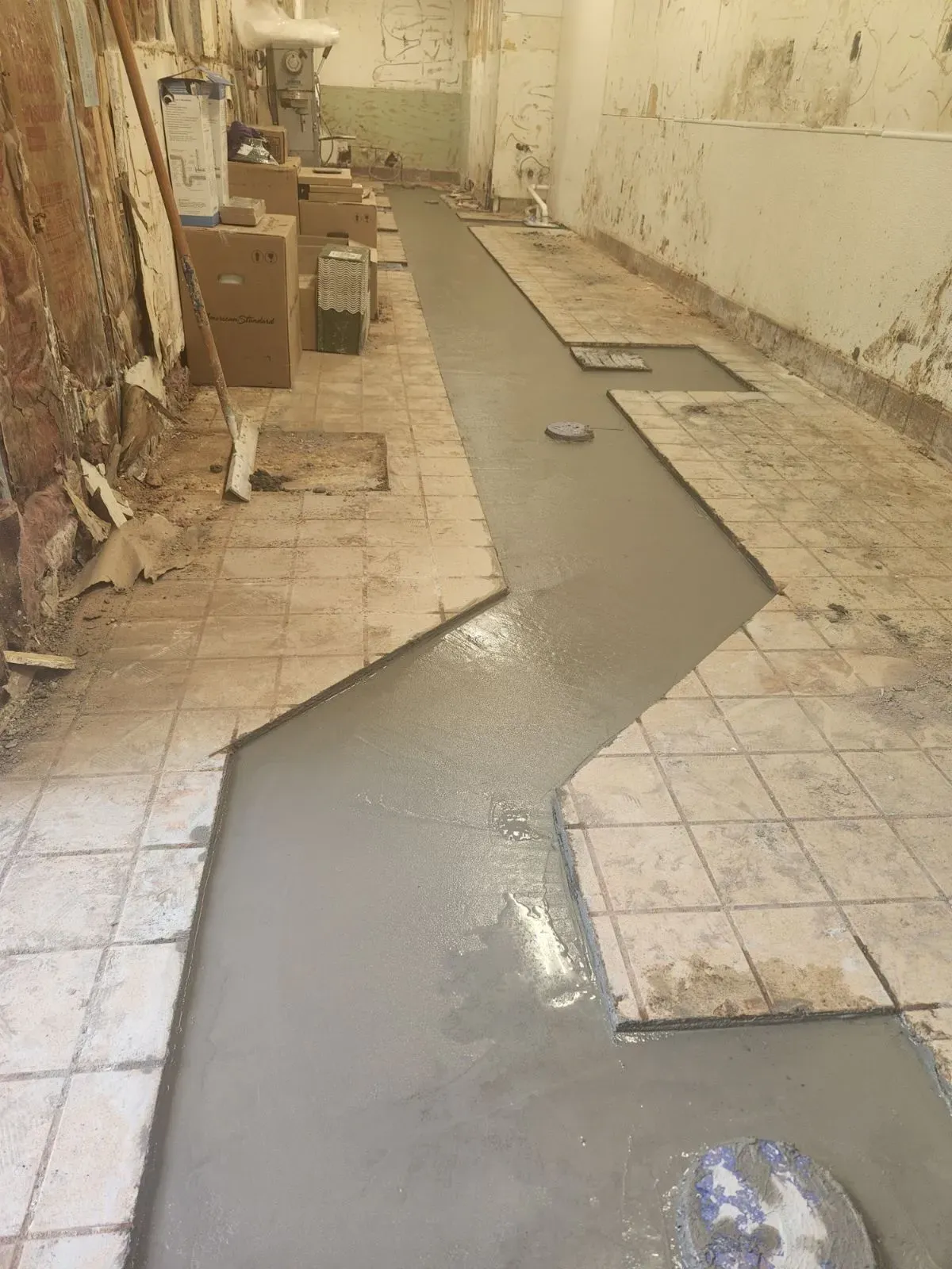 Construction in a long, narrow room. Gray concrete covers the floor; walls are exposed brick.