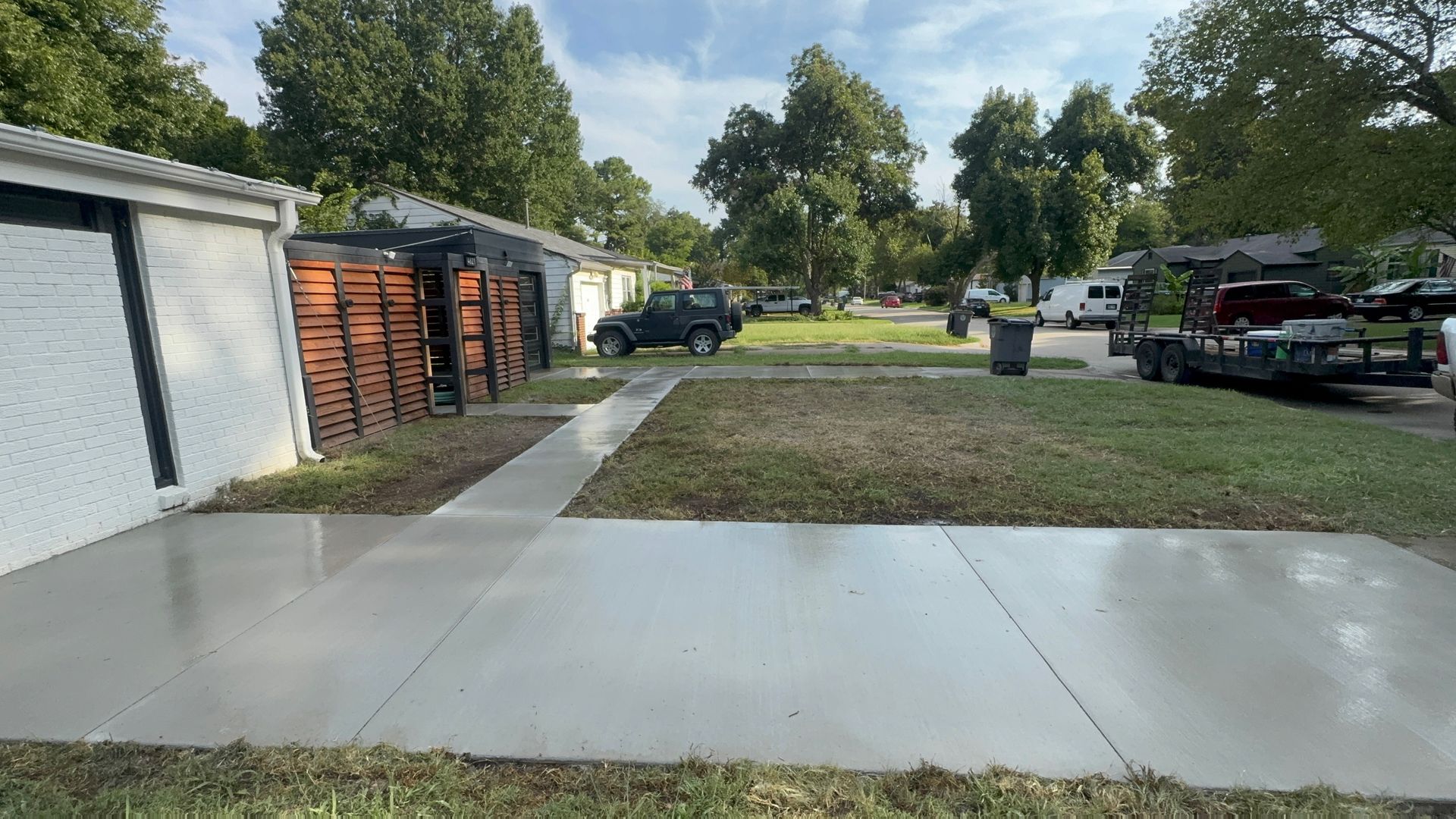 Concrete driveway beside garage with parked vehicles and trees along a grassy lot