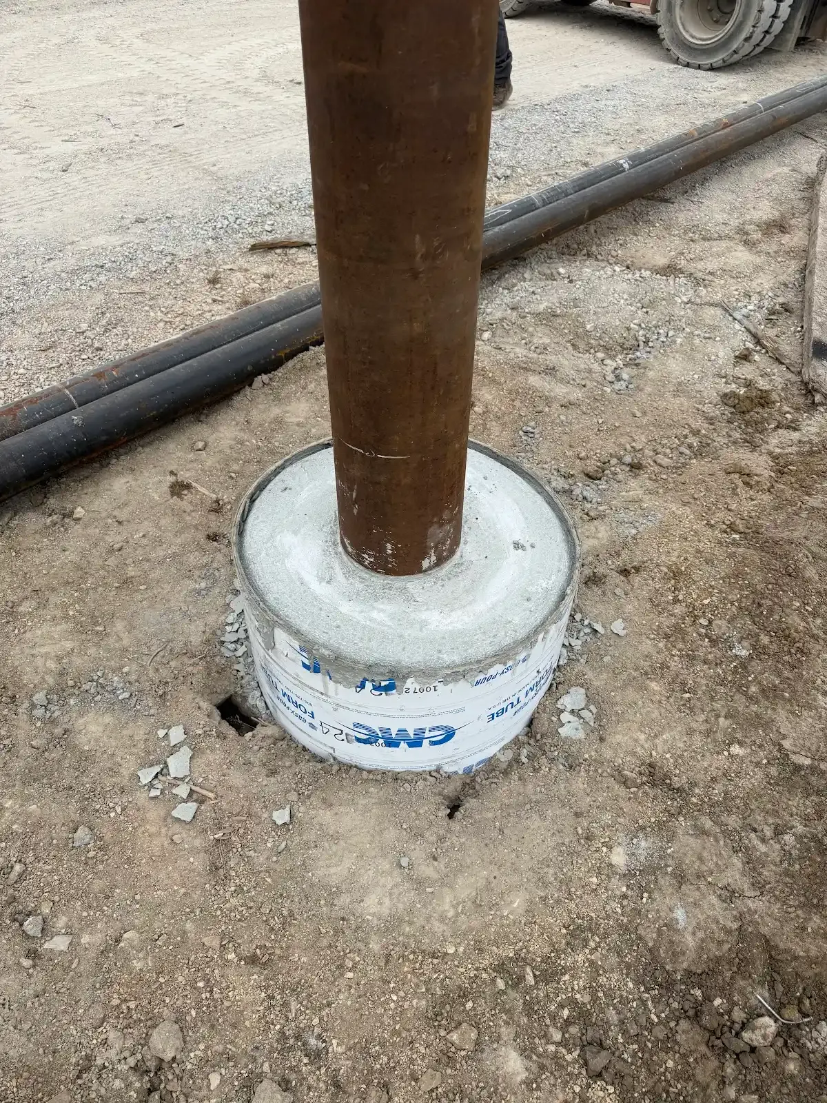 A metal pipe is embedded in a concrete base, set in a dirt and gravel ground.