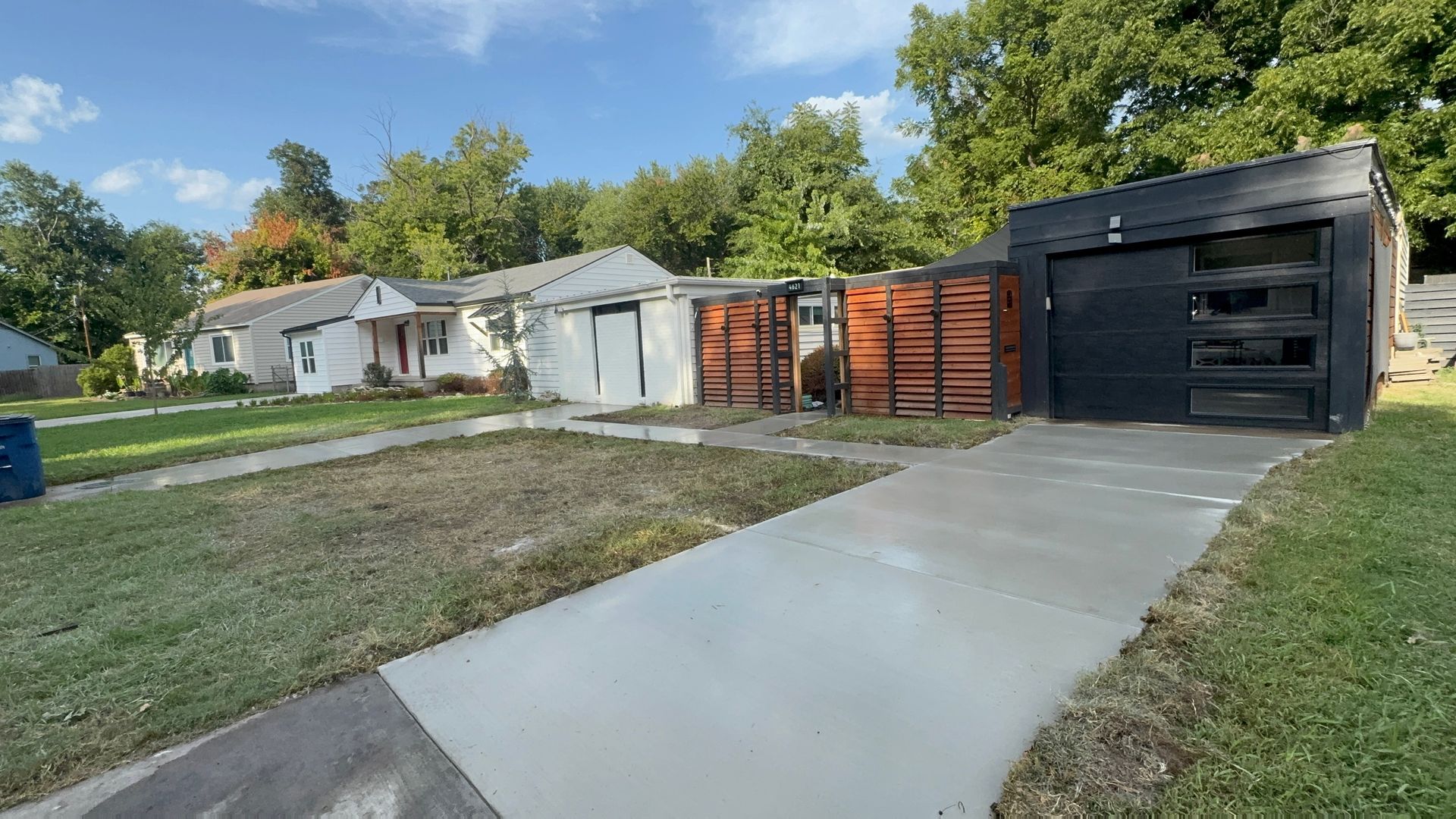Suburban driveway leading to garages and a white house, with a blue sky and grassy yard.