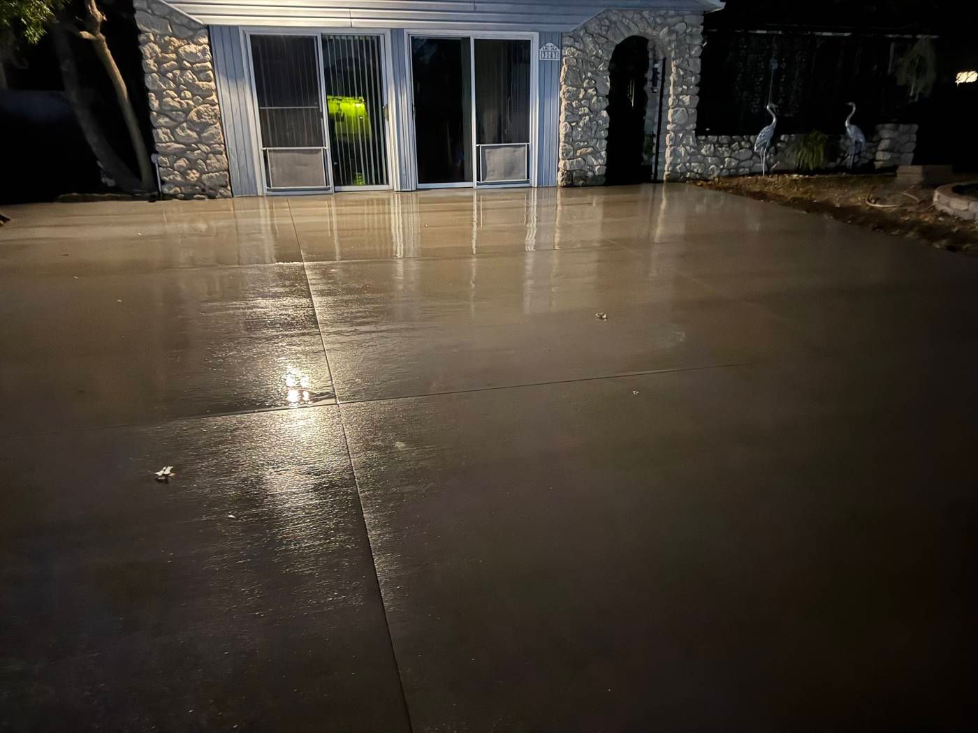 Rain-slick concrete driveway at night in front of a stone building with glass doors