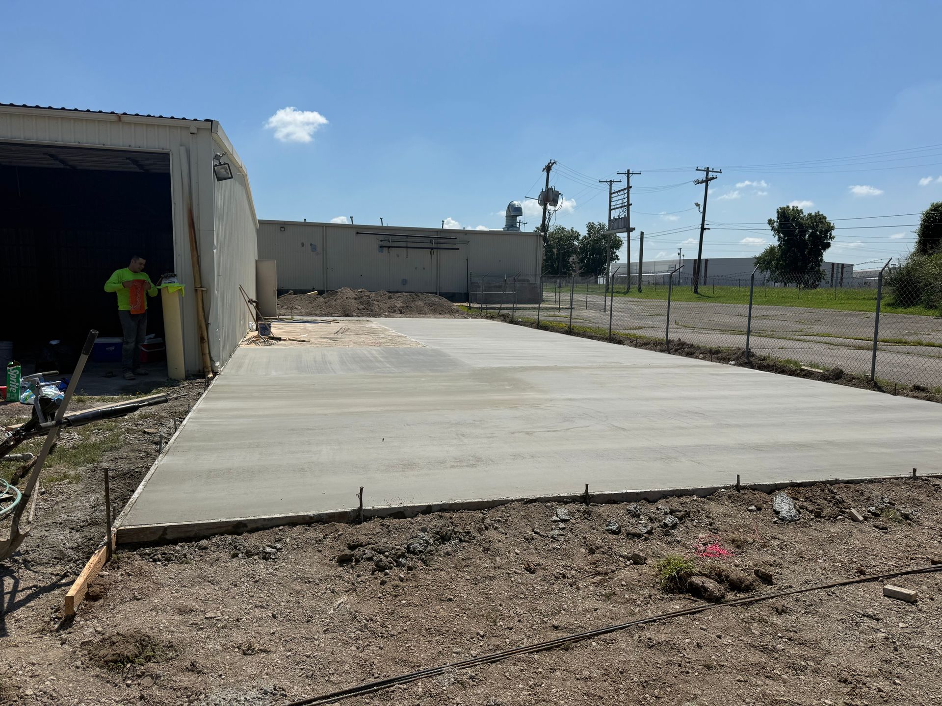 Concrete slab in a rural lot beside a garage, with a person working at the left edge.