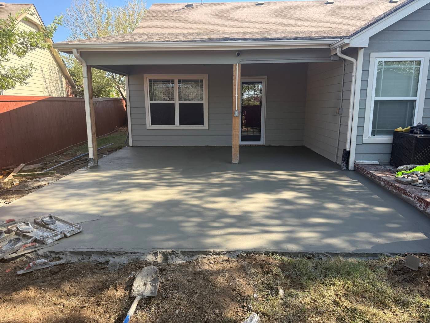 Backyard patio and concrete slab beside a house with a covered porch and window