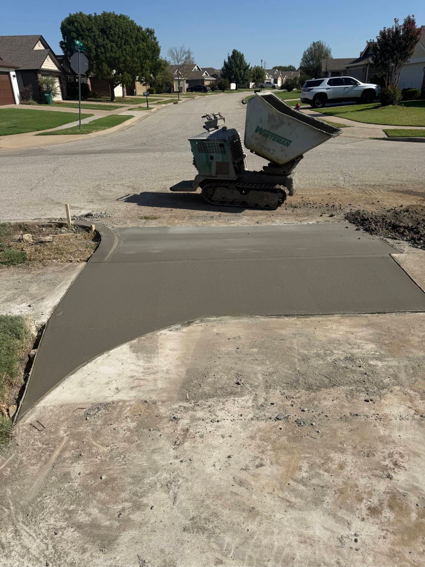 Broken sidewalk ramp at a street curb, with a utility box and dumpster across a residential road.